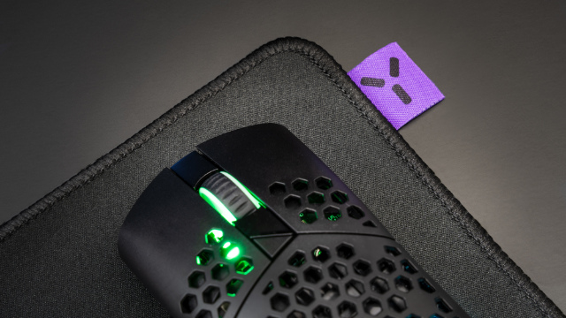 Souris de jeu noire sur un tapis de souris noir avec une étiquette violette. La souris a des lumières vertes.