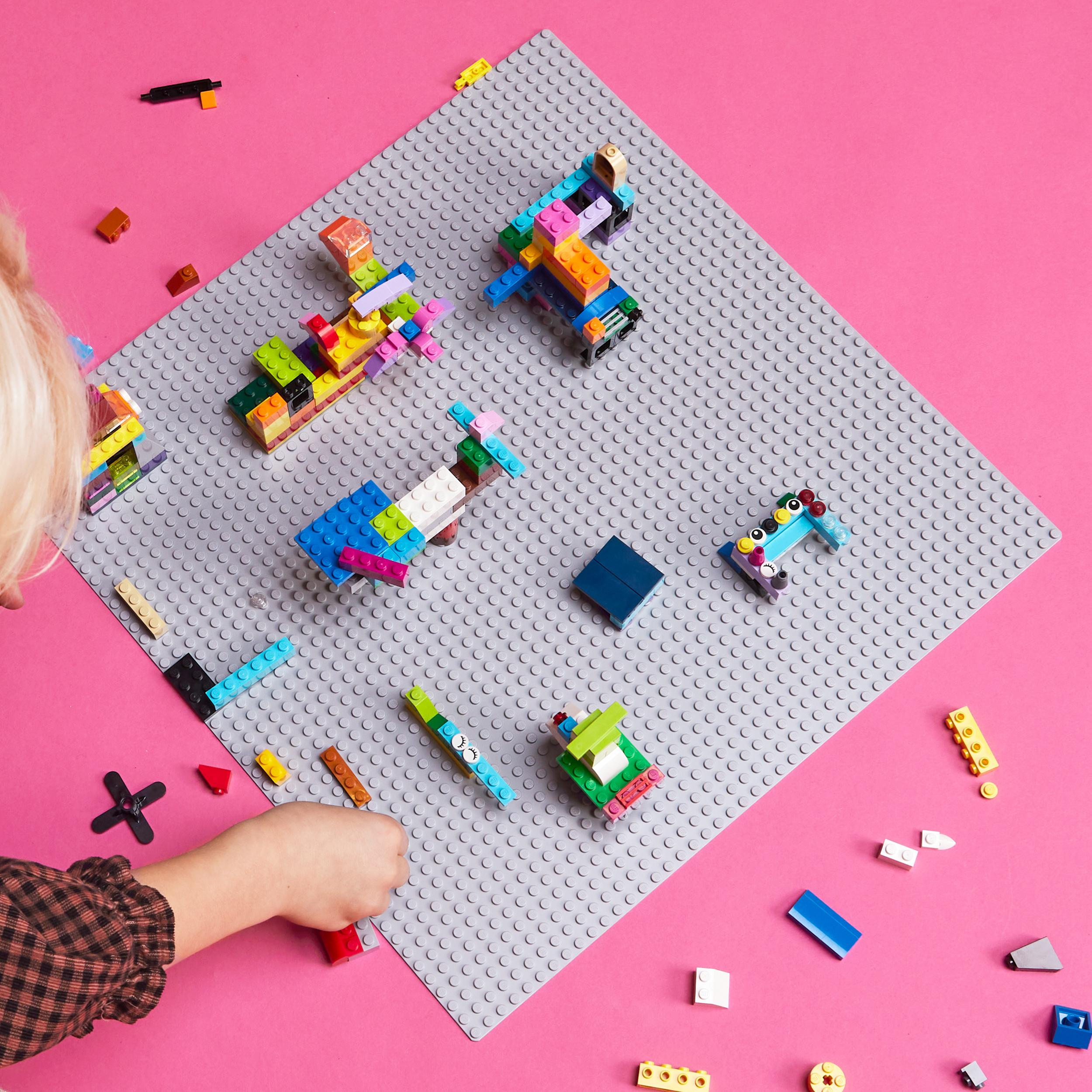 Ein Kind spielt mit Lego-Steinen auf einer rosa Oberfläche. Verschiedene Lego-Kreationen sind verstreut.
