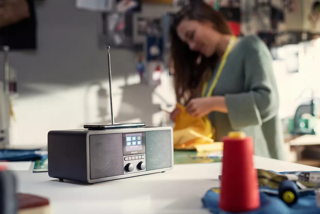 Une radio et un téléphone sont sur une table. Une femme est à l'arrière-plan.
