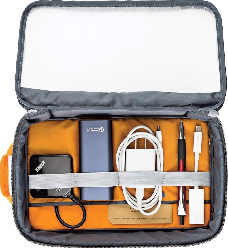 Borsa organizer da viaggio aperta, piena di accessori tecnologici. Interno arancione, zip bianca.