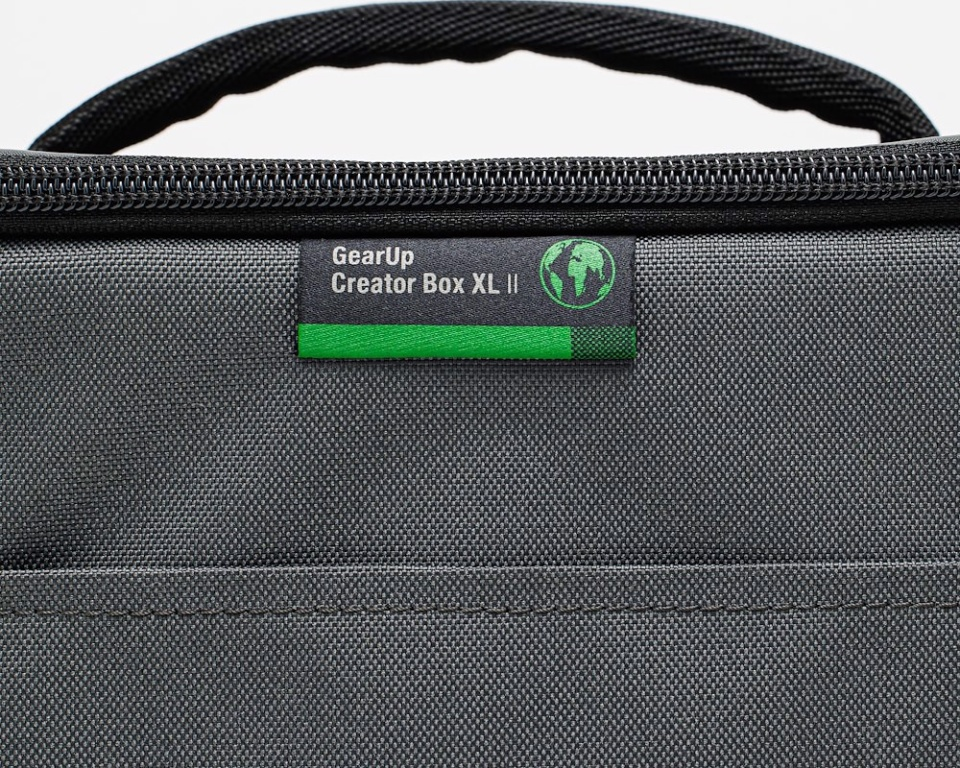 Gros plan sur un sac gris avec une poignée et une fermeture éclair noires. Il porte une étiquette verte et noire indiquant GearUp Creator Box XL II.
