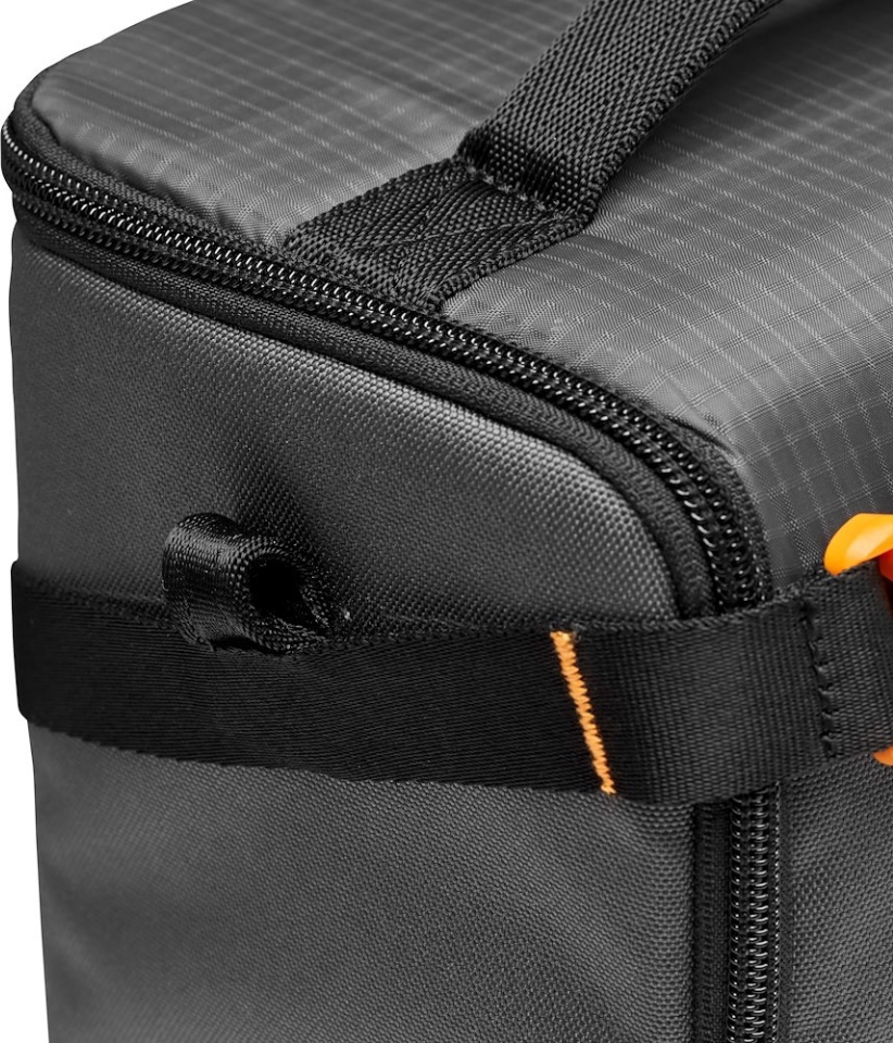 Gros plan sur un sac noir avec fermeture éclair, sangle et poignée. Un clip orange est visible. Le sac a une surface texturée.