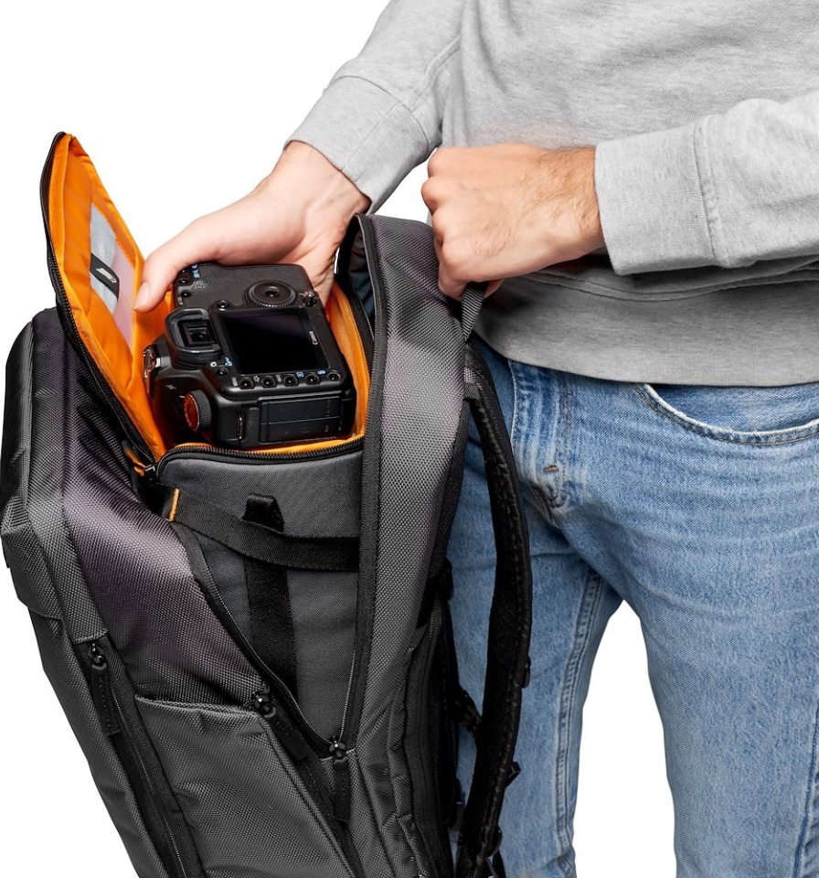Une personne place un appareil photo noir dans un sac à dos gris. Le sac à dos a un intérieur orange.