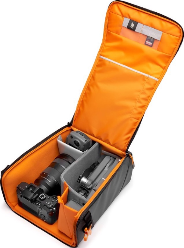 Sac photo ouvert avec appareil photo, objectif, drone et accessoires. Intérieur orange, extérieur gris. Articles bien rangés.