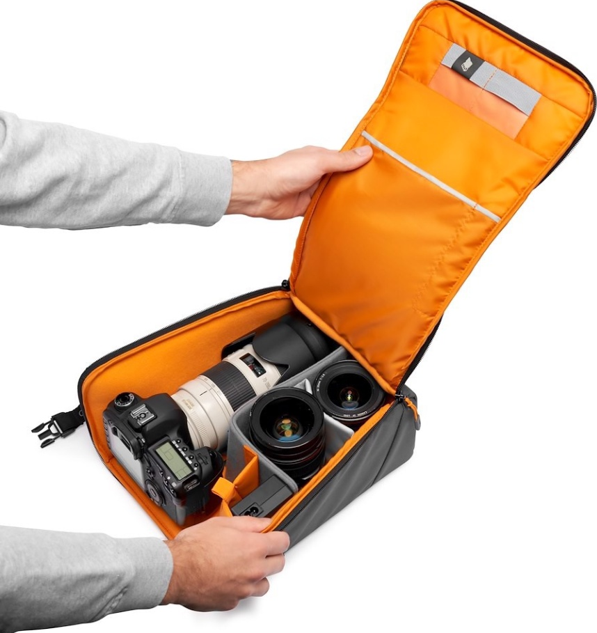 Sac photo ouvert avec appareil photo et objectifs. Intérieur orange, extérieur gris. Mains tenant le sac ouvert, fond blanc.