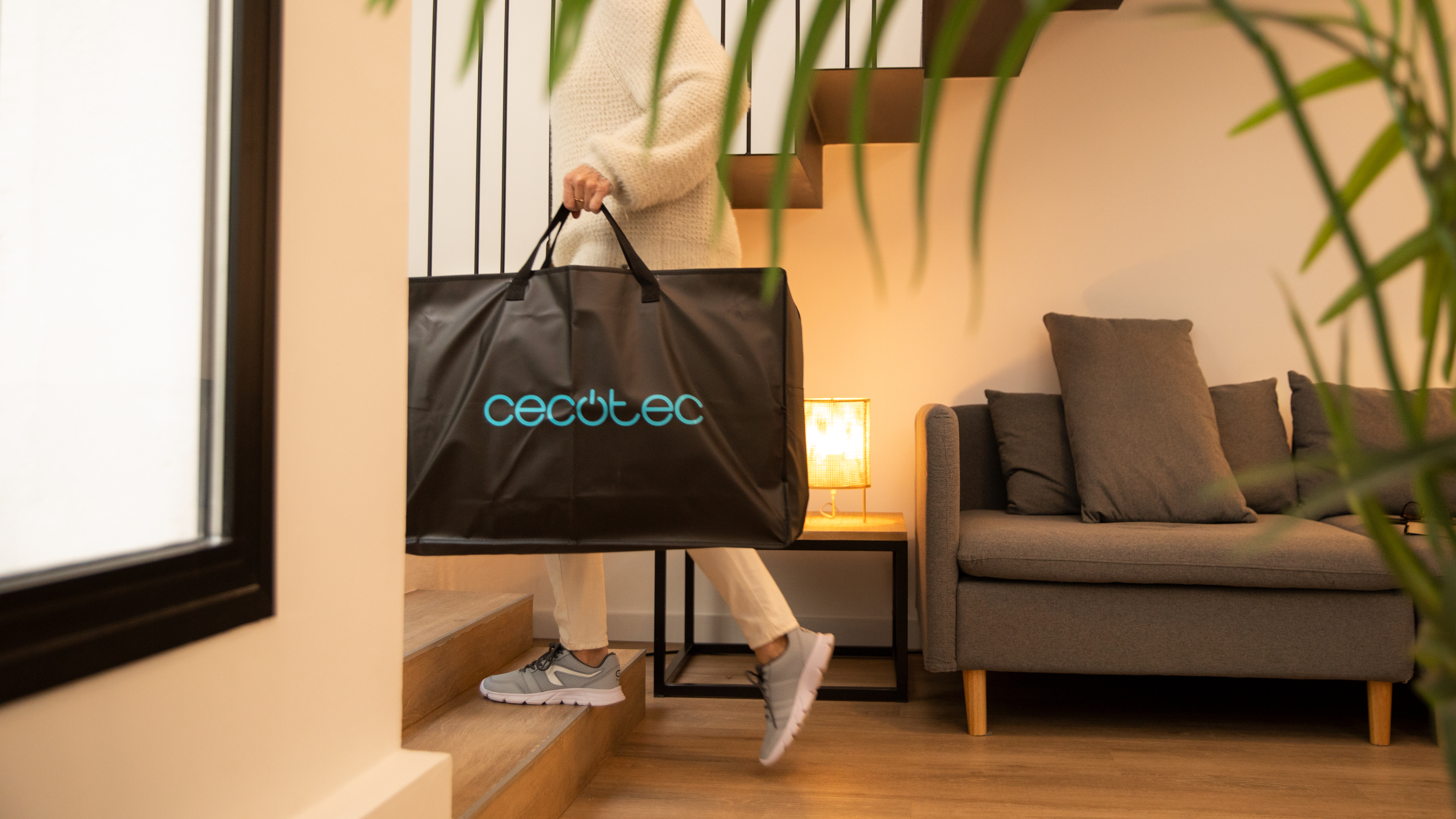 Una mujer lleva una bolsa de compras negra con el logo 'cecotec' subiendo las escaleras.