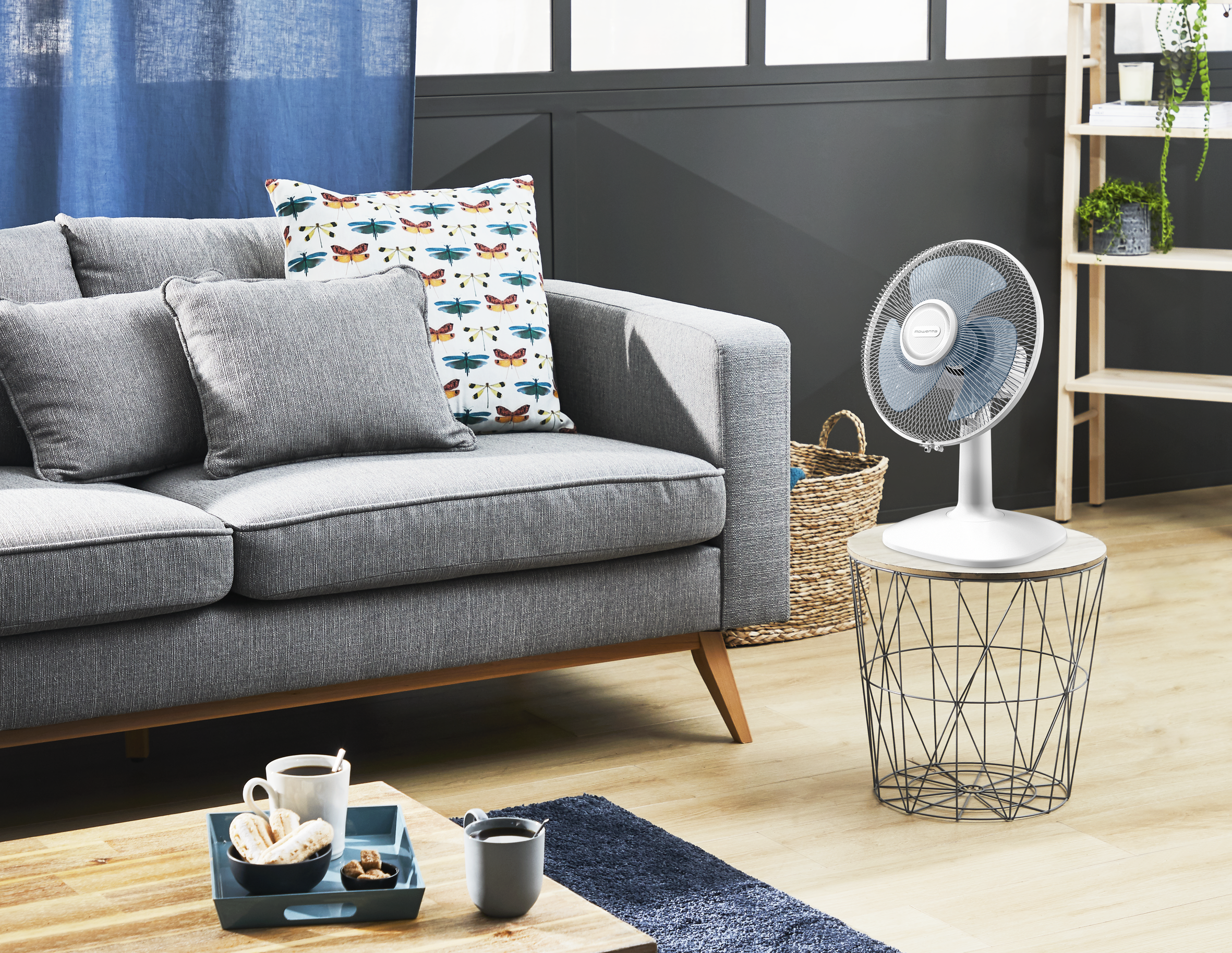 Una sala de estar con sofá, ventilador y mesa de centro. Dominan los tonos azules y grises.