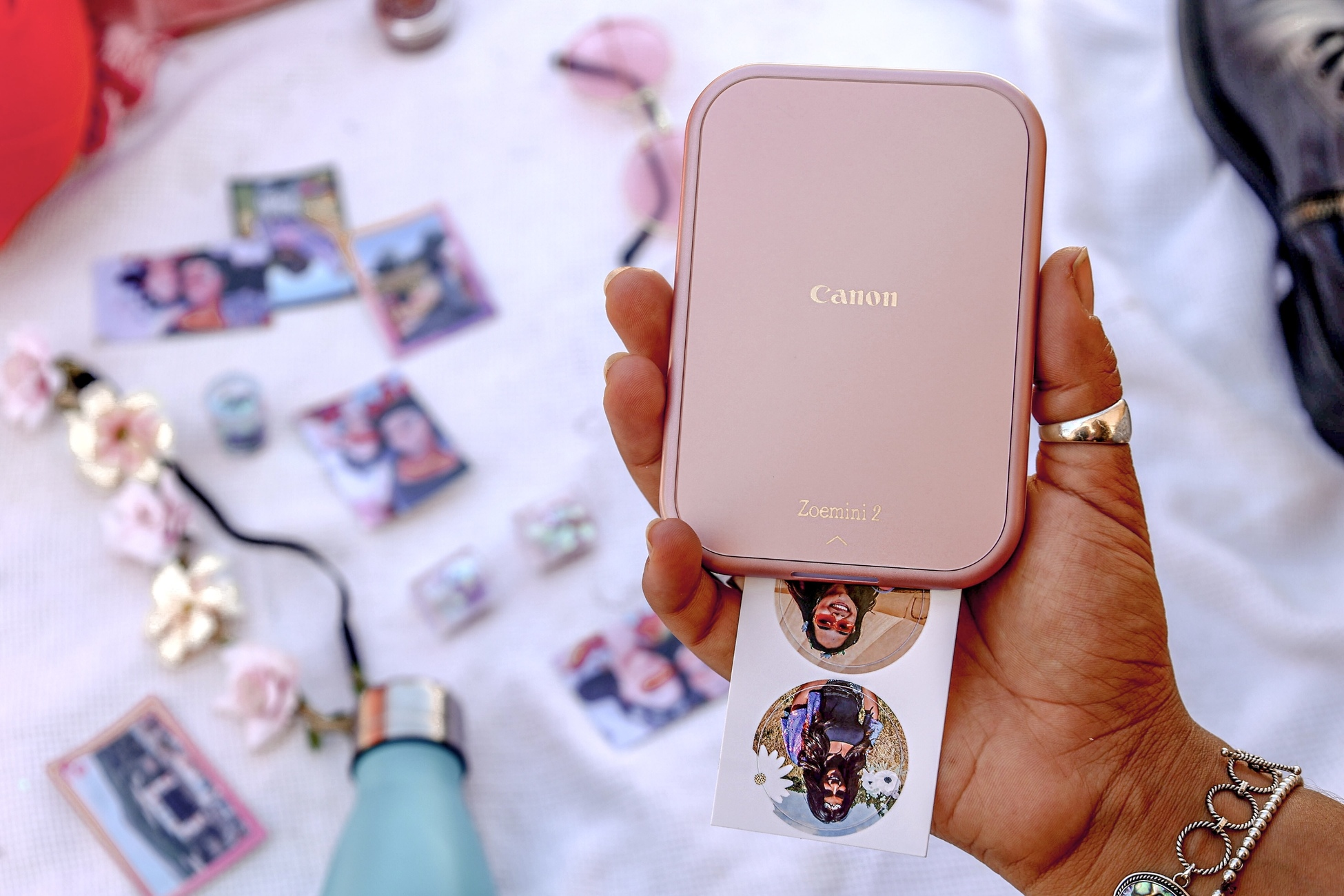 Frau hält eine pinke Canon Zoemini 2. Fotos sind auf einer weißen Oberfläche verstreut.