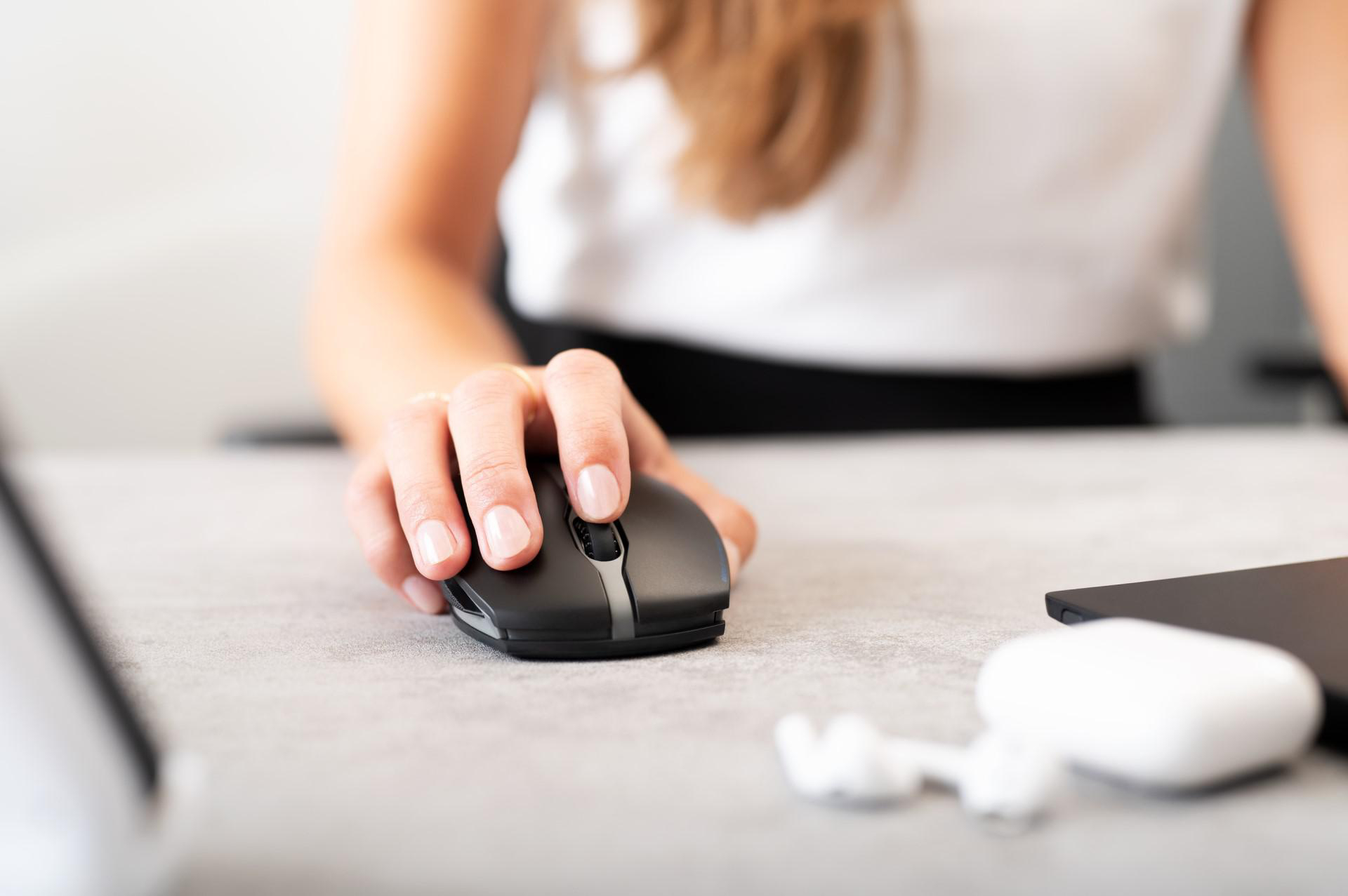 Frauenhand benutzt eine schwarze Computermaus auf einem hellgrauen Schreibtisch.