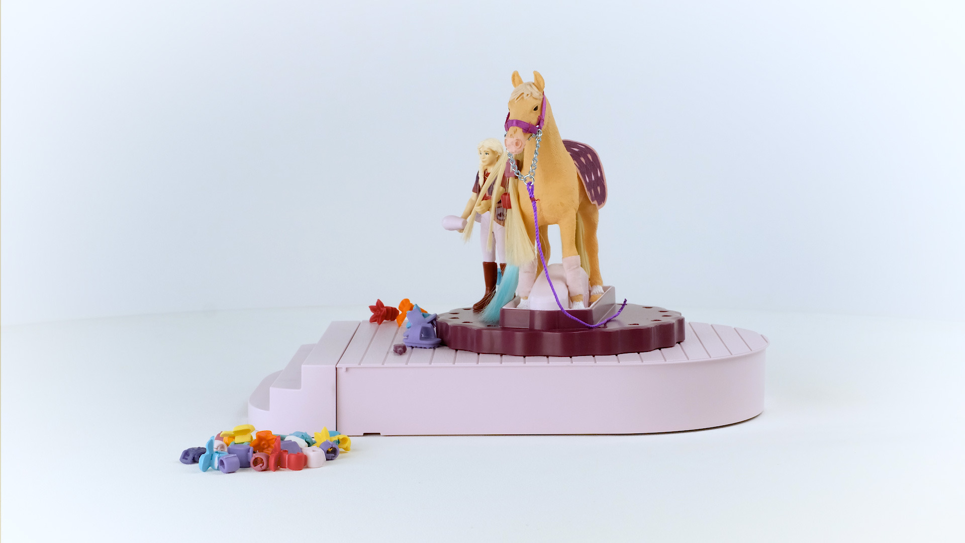Ein Spielzeugset mit zwei Puppen, einem Pferd und Zubehör auf einer rosa Basis.