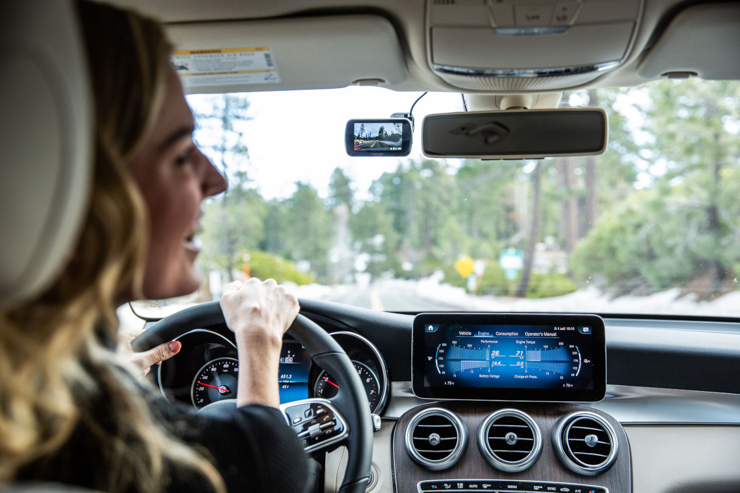 Une femme conduit une voiture, tenant le volant. L'intérieur de la voiture est visible.