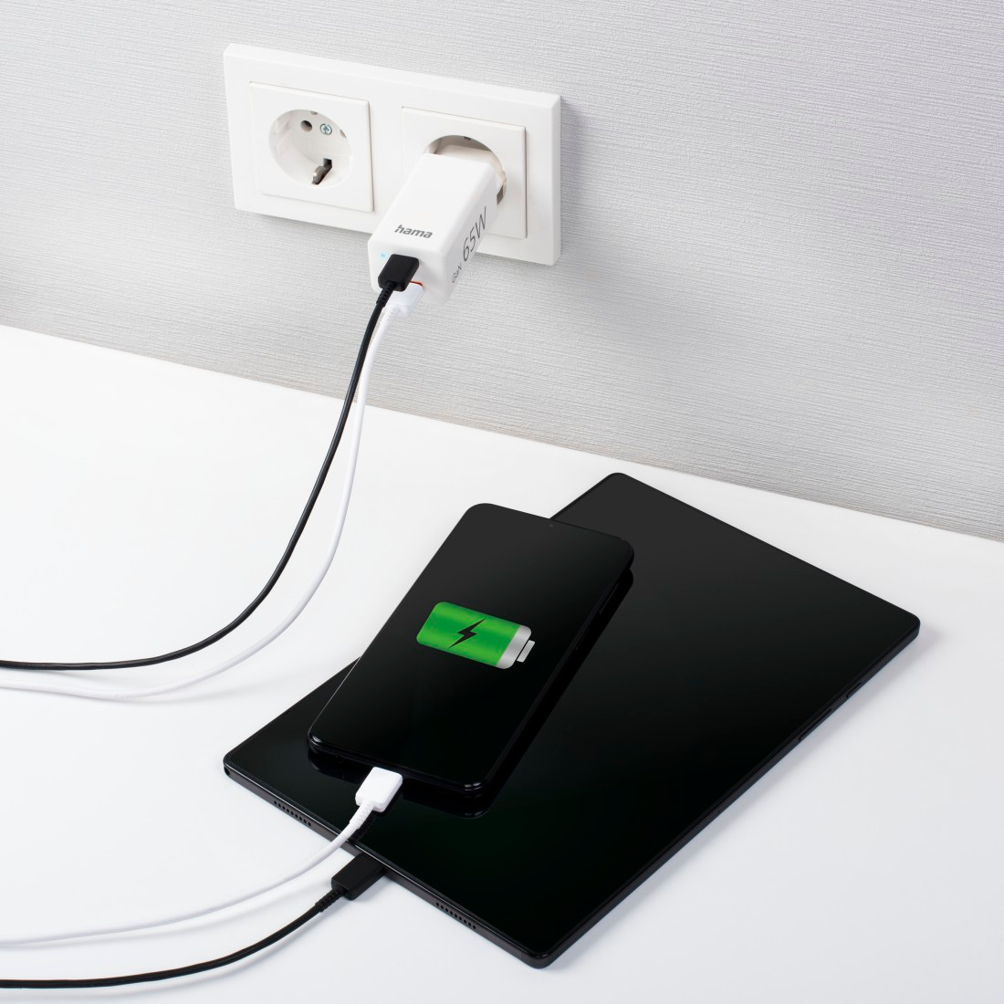 Phone charging with a wall charger and tablet on a white surface.