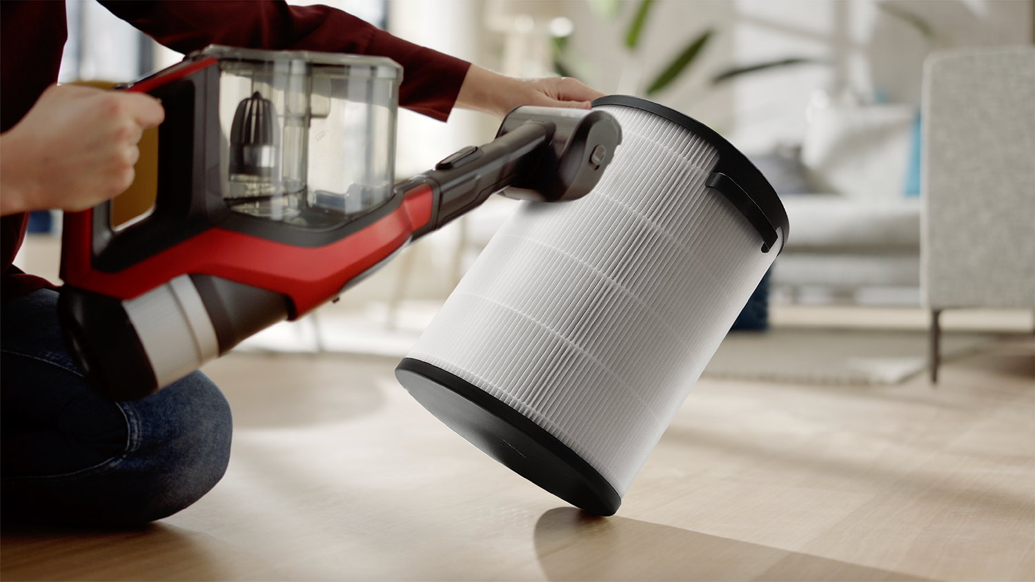 A person is changing the filter of a red and black vacuum cleaner.