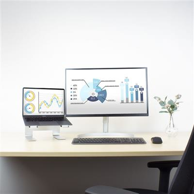 A laptop on a stand, a large monitor, keyboard, mouse, and a small plant on a desk against a white wall.