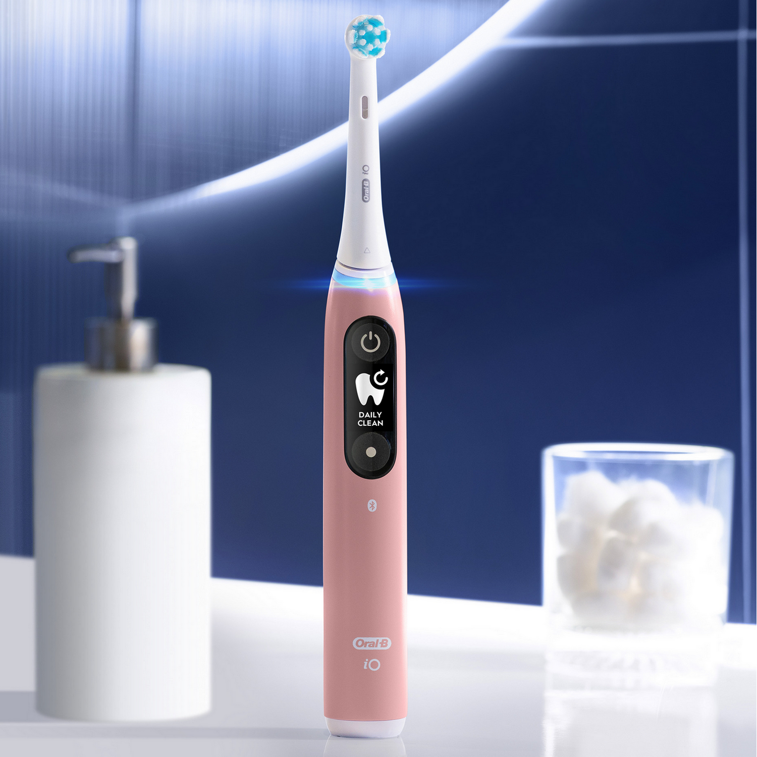 Pink electric toothbrush with a screen and a white soap dispenser beside it.