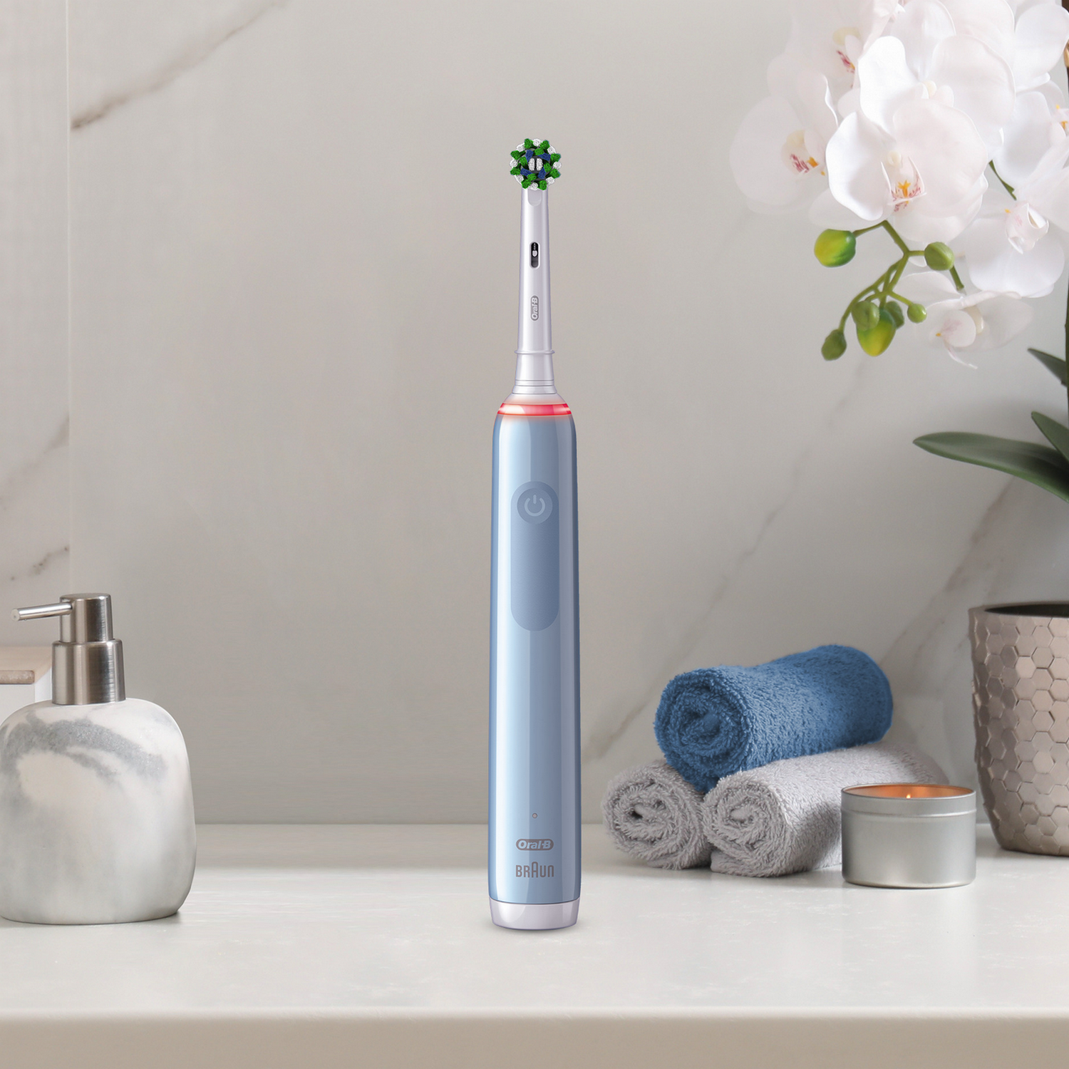 Blauwe elektrische tandenborstel op een aanrecht met een zeepdispenser, handdoeken en bloemen.