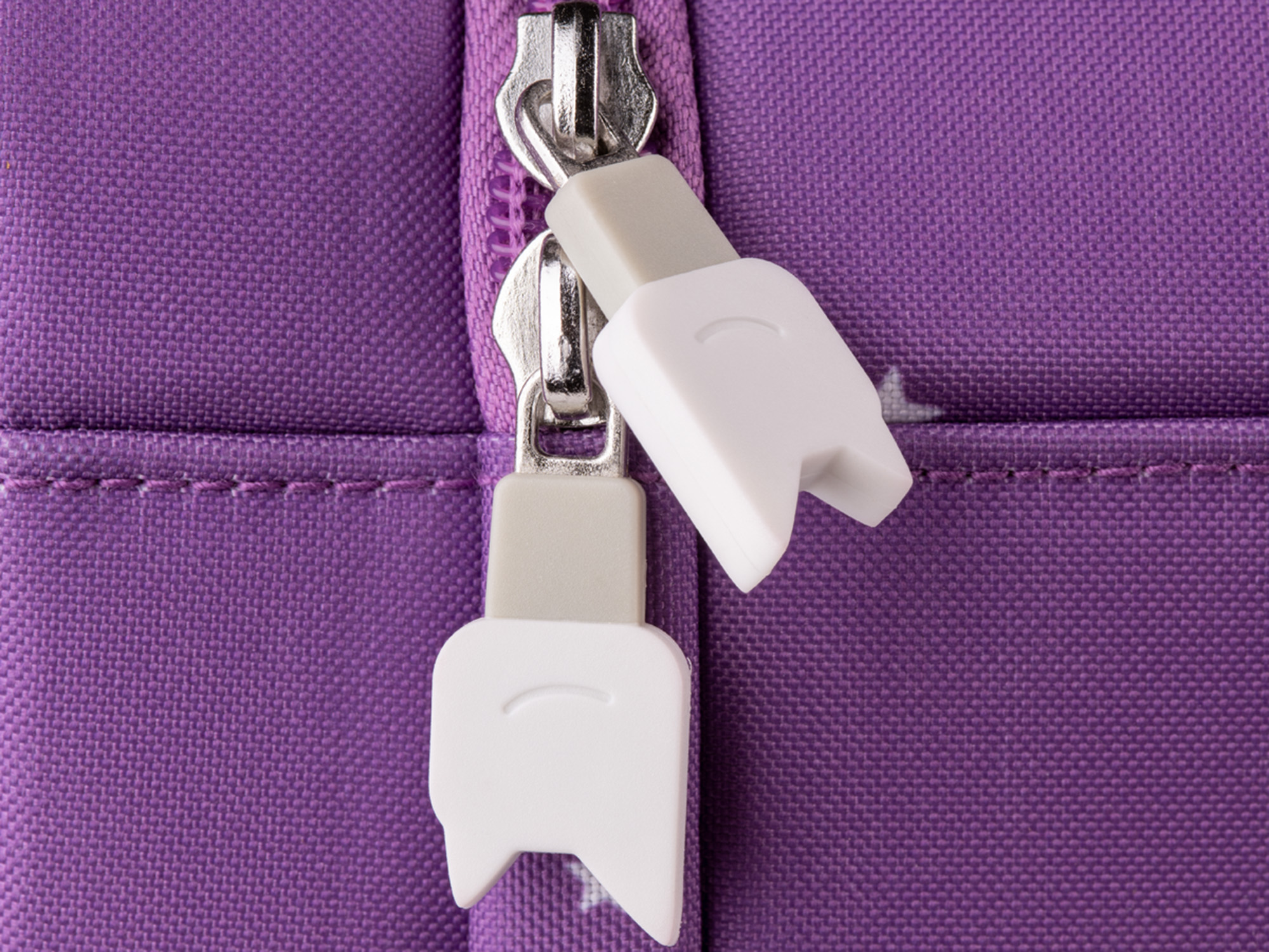 Nahaufnahme eines Reißverschlusses an einer lila Tasche. Weiße Reißverschlusszieher mit Zahndesign.
