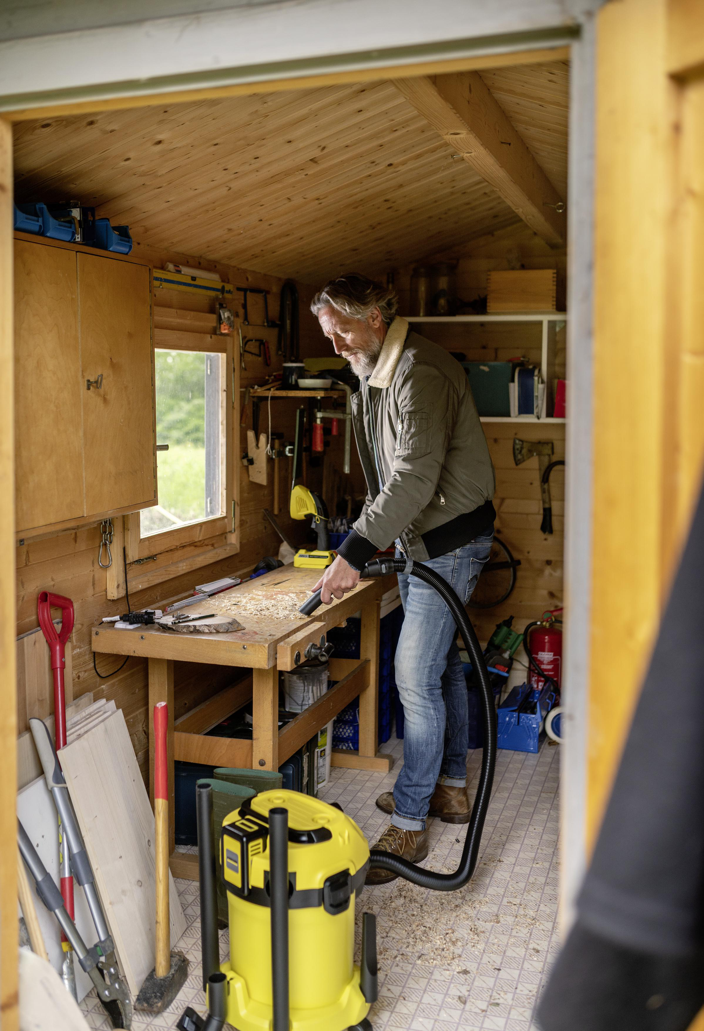 Mann in einem Schuppen, der Holzspäne mit einem gelben Staubsauger saugt.