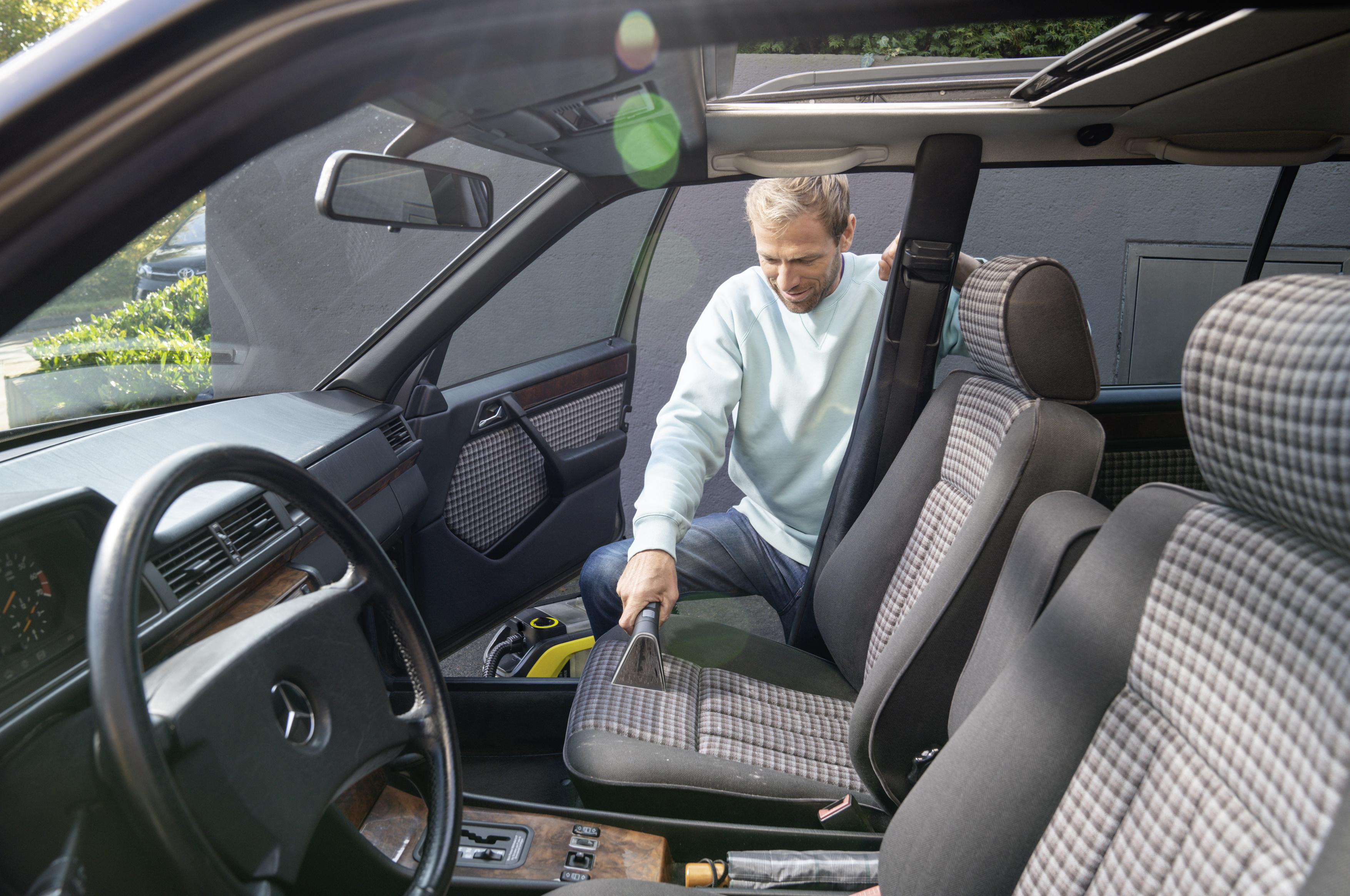 Ein Mann saugt den Innenraum eines Autos. Die Szene ist durch die Windschutzscheibe.