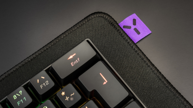 Esquina del teclado con tecla Entf resaltada. Superficie negra. Etiqueta morada con símbolo en la esquina.
