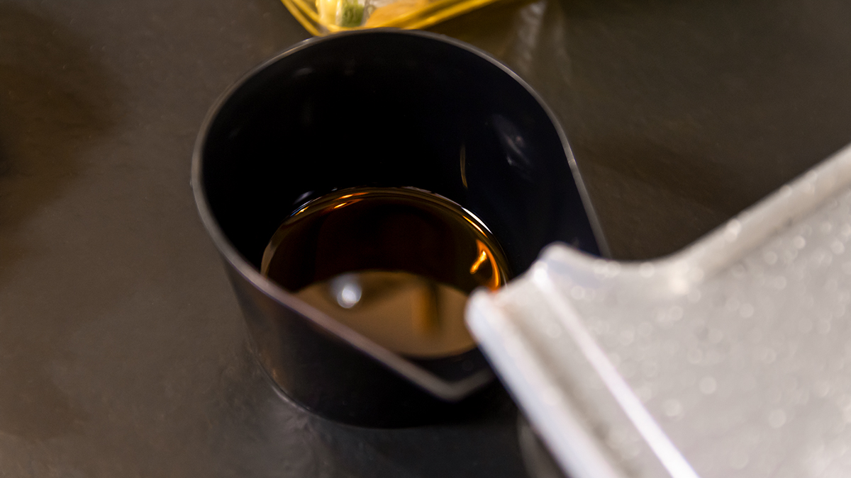 Un vaso medidor negro contiene un líquido oscuro. Una bandeja plateada es parcialmente visible a la derecha.