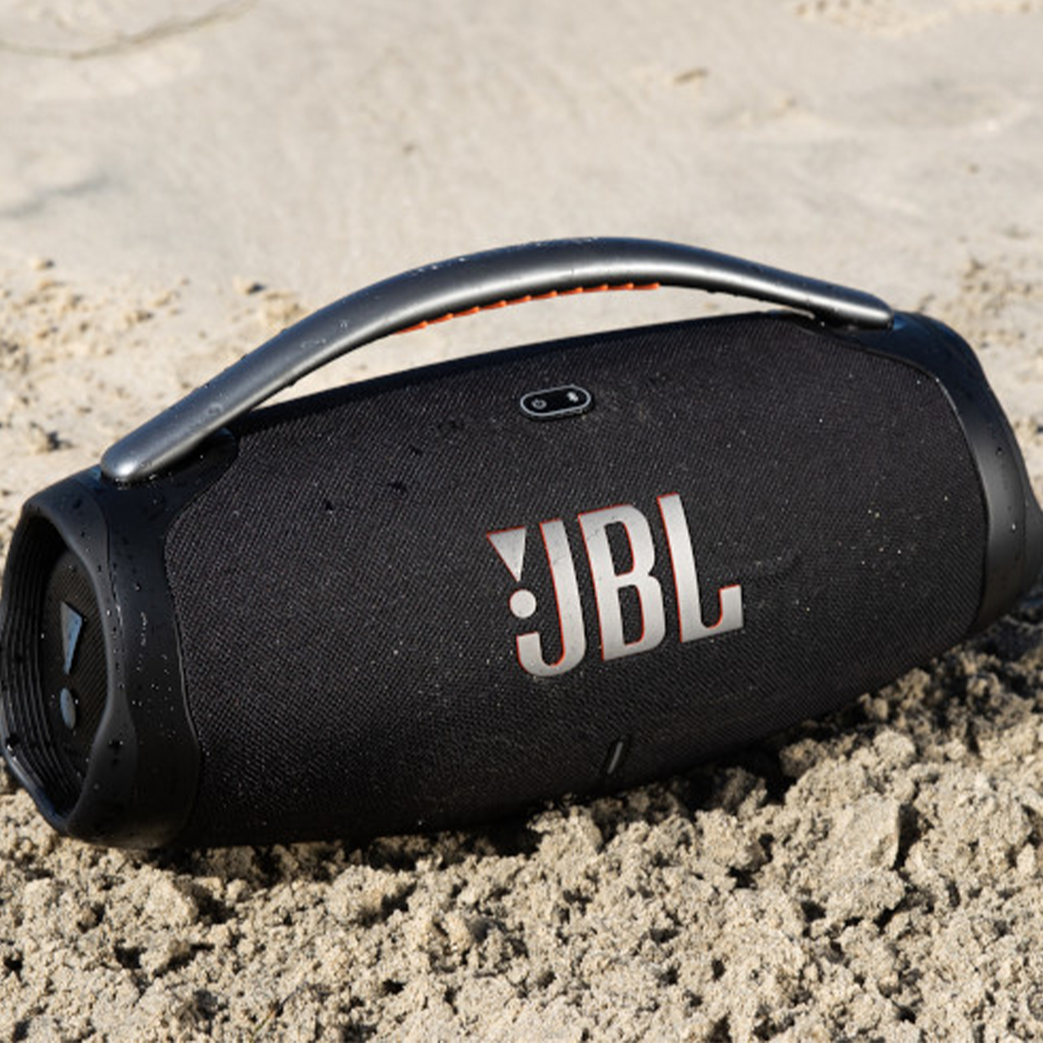 Un altoparlante JBL nero sulla sabbia, con maniglia e logo. Sabbia sullo sfondo.