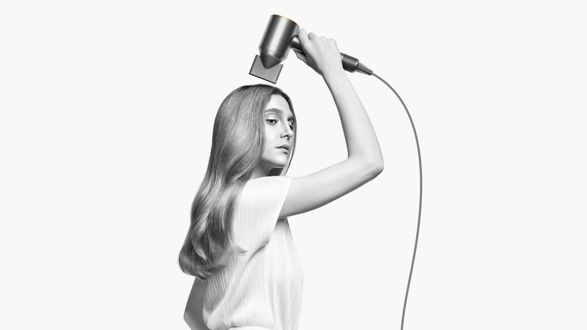 Dyson saç kurutma makinesi kullanan kadın, başının üzerinde tutuyor. Beyaz zemin.