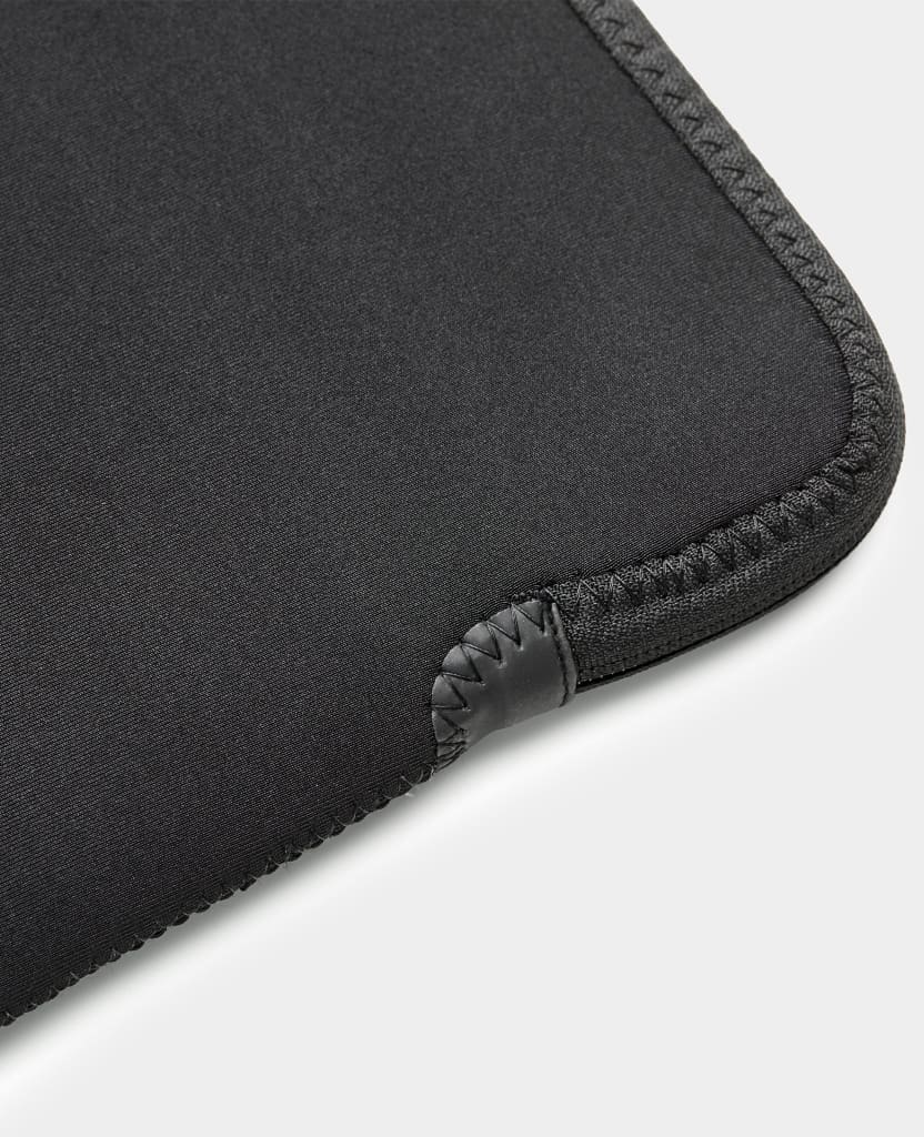 Eine schwarze Neoprenhülle für ein Gerät. Die Ecke ist mit einem Lederaufnäher vernäht. Weißer Hintergrund.