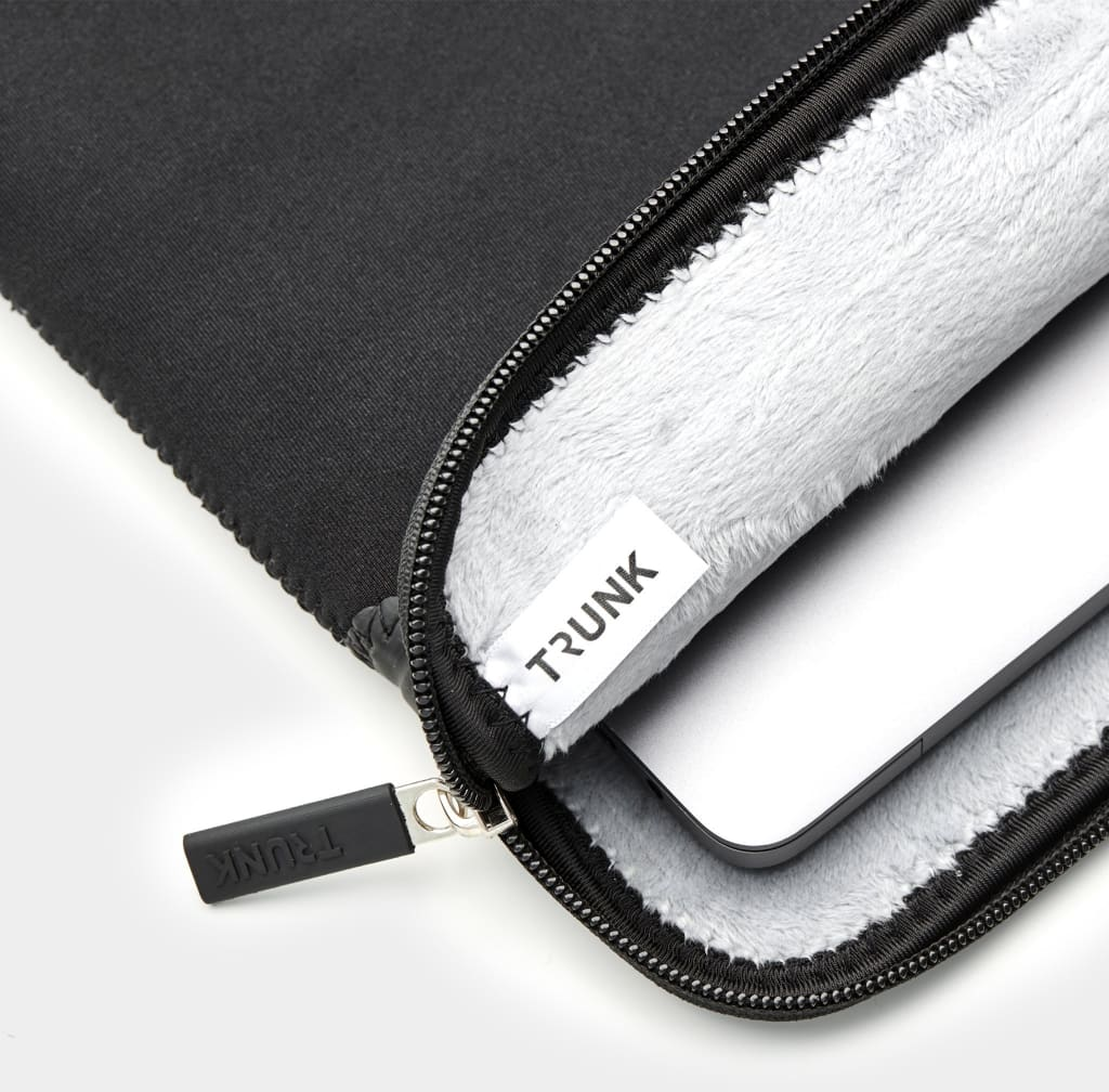 Schwarze Laptoptasche mit Reißverschluss. Innen weich, weiß, TRUNK-Etikett sichtbar.