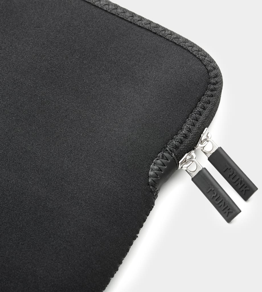Nahaufnahme einer schwarzen Laptoptasche mit zwei silbernen Reißverschlüssen. Das Wort „TRUNK“ steht drauf.