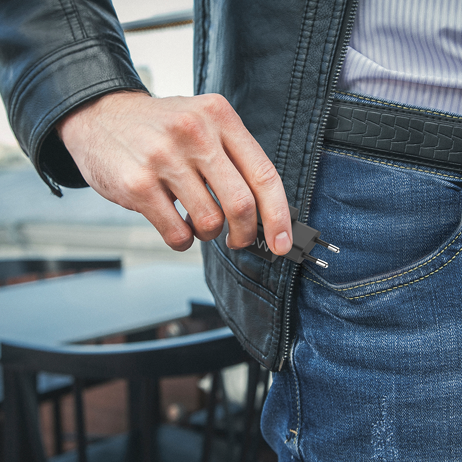 A man in a jacket and jeans is pulling a black plug from his pocket.