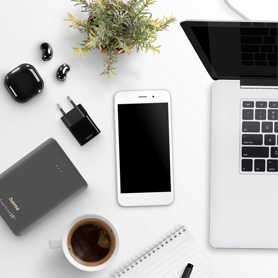 White desk with phone, power bank, charger, headphones, and coffee.