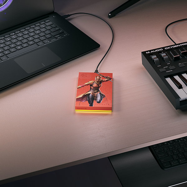 Una computadora portátil, un disco duro externo y un teclado en un escritorio. El disco duro tiene un diseño gráfico.