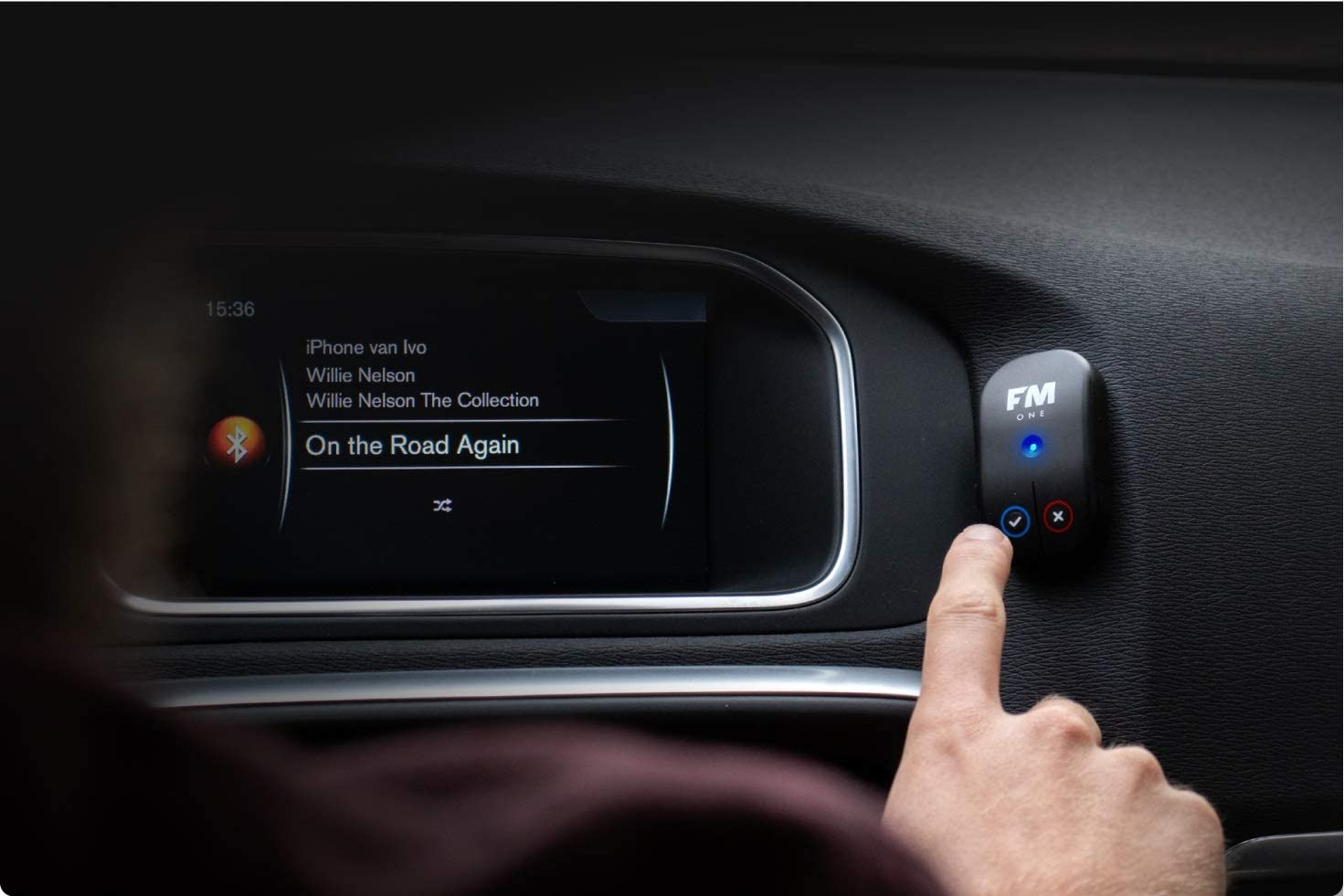 FM ONE-apparaat in een auto, hand drukt op knop, autoscherm zichtbaar.