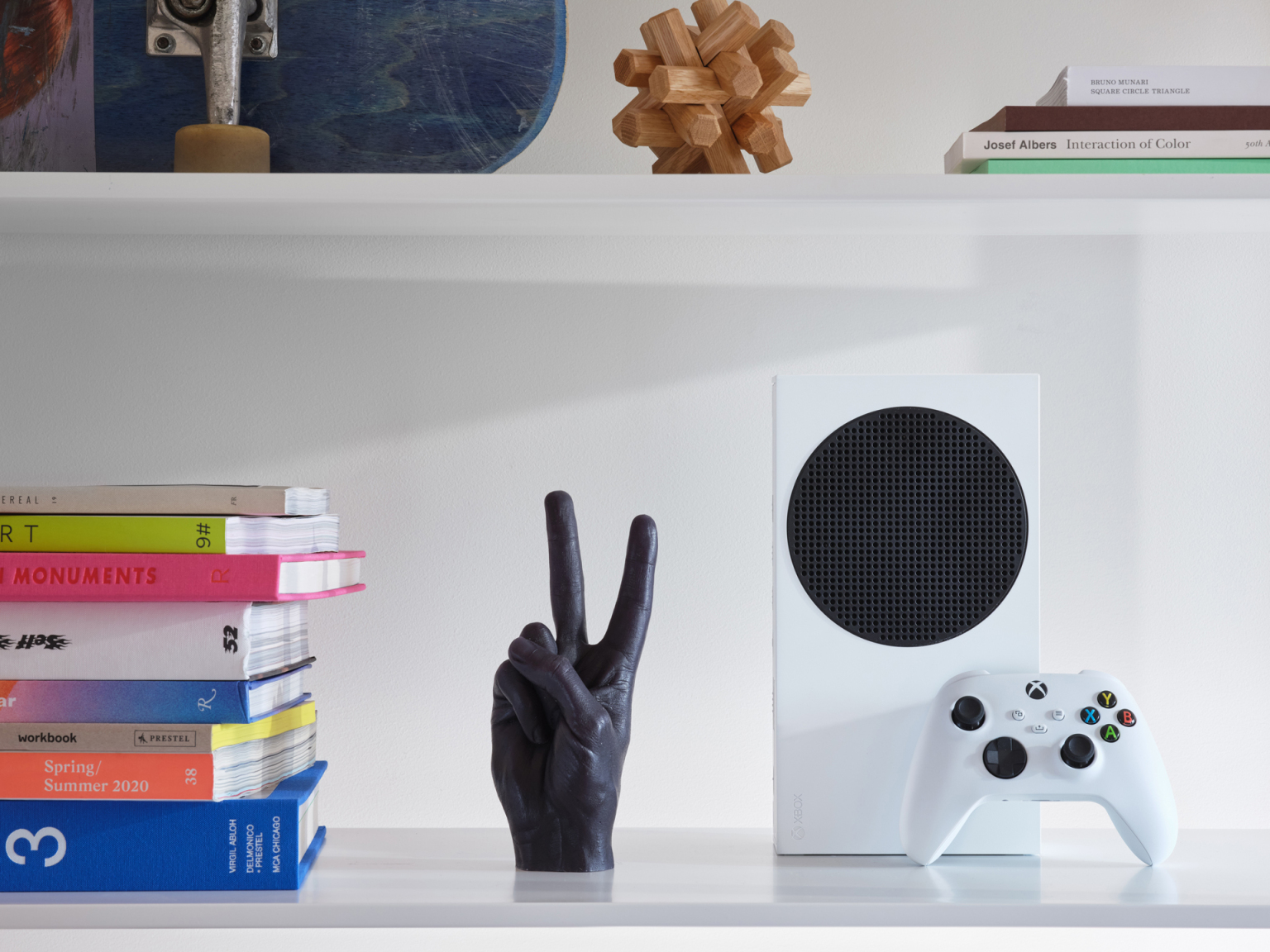 Une étagère avec des livres, une sculpture de main noire, une console Xbox blanche et une manette.