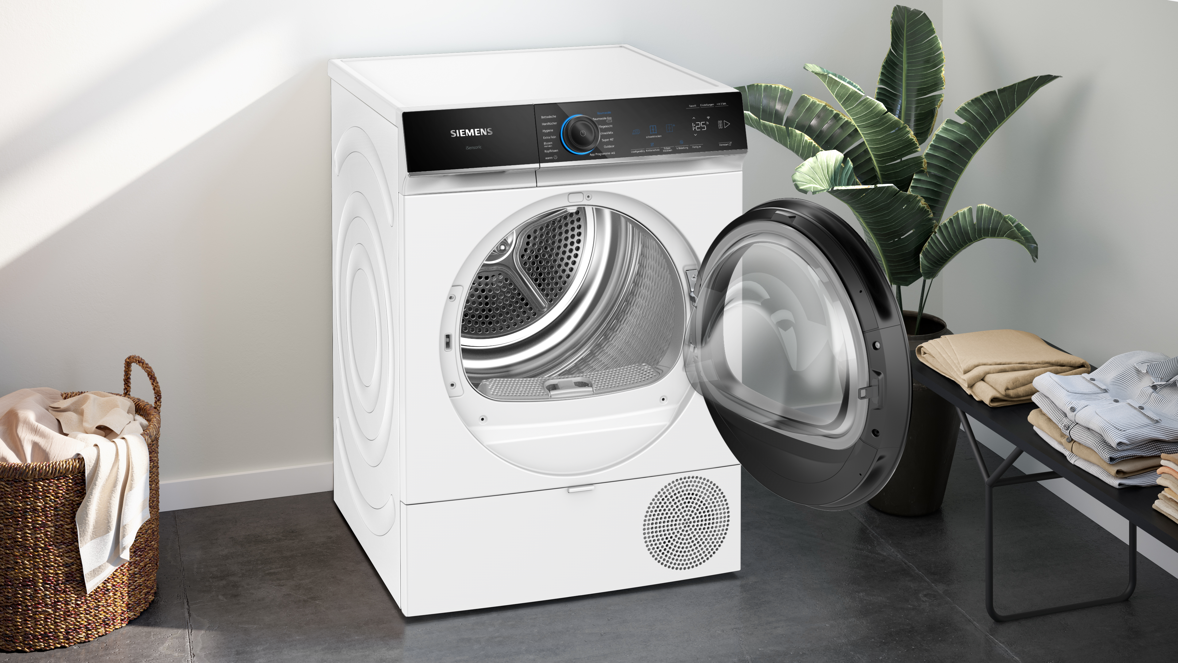 Ein weißer Siemens-Trockner mit offener Tür, einer Pflanze und gefalteter Kleidung. Ein Korb mit Kleidung im Vordergrund.