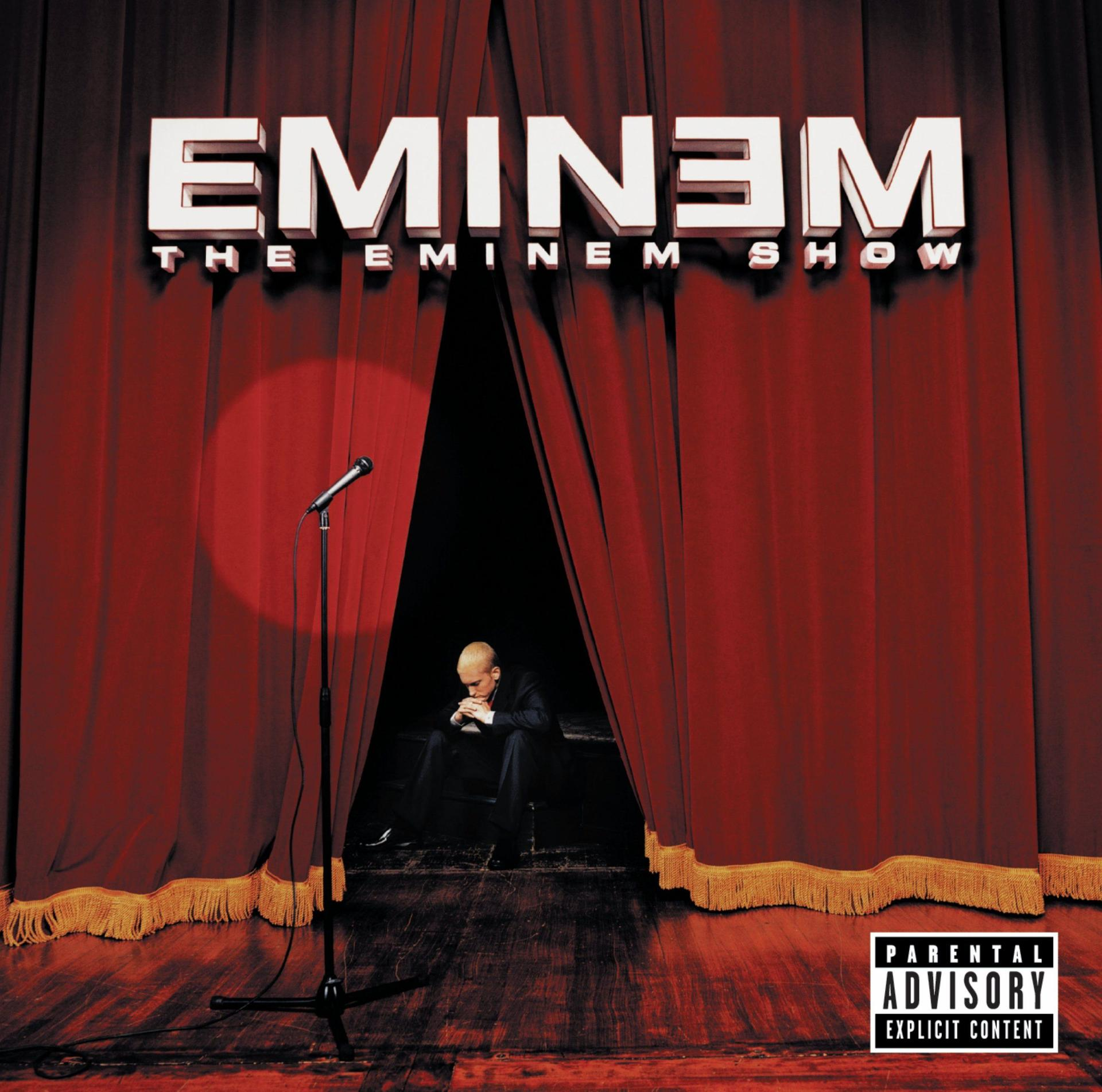 Eminem album borítója. Eminem fekete öltönyben ül a színpadon. Piros függöny és mikrofon.
