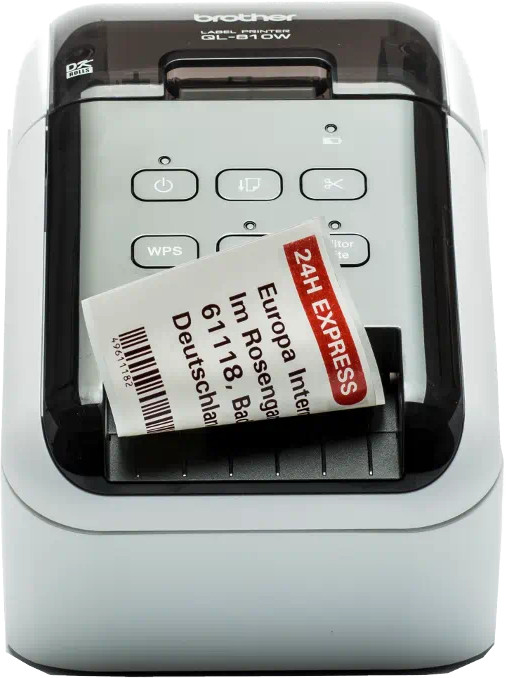 A white and gray label printer with a label exiting the slot. The label has text and a barcode.