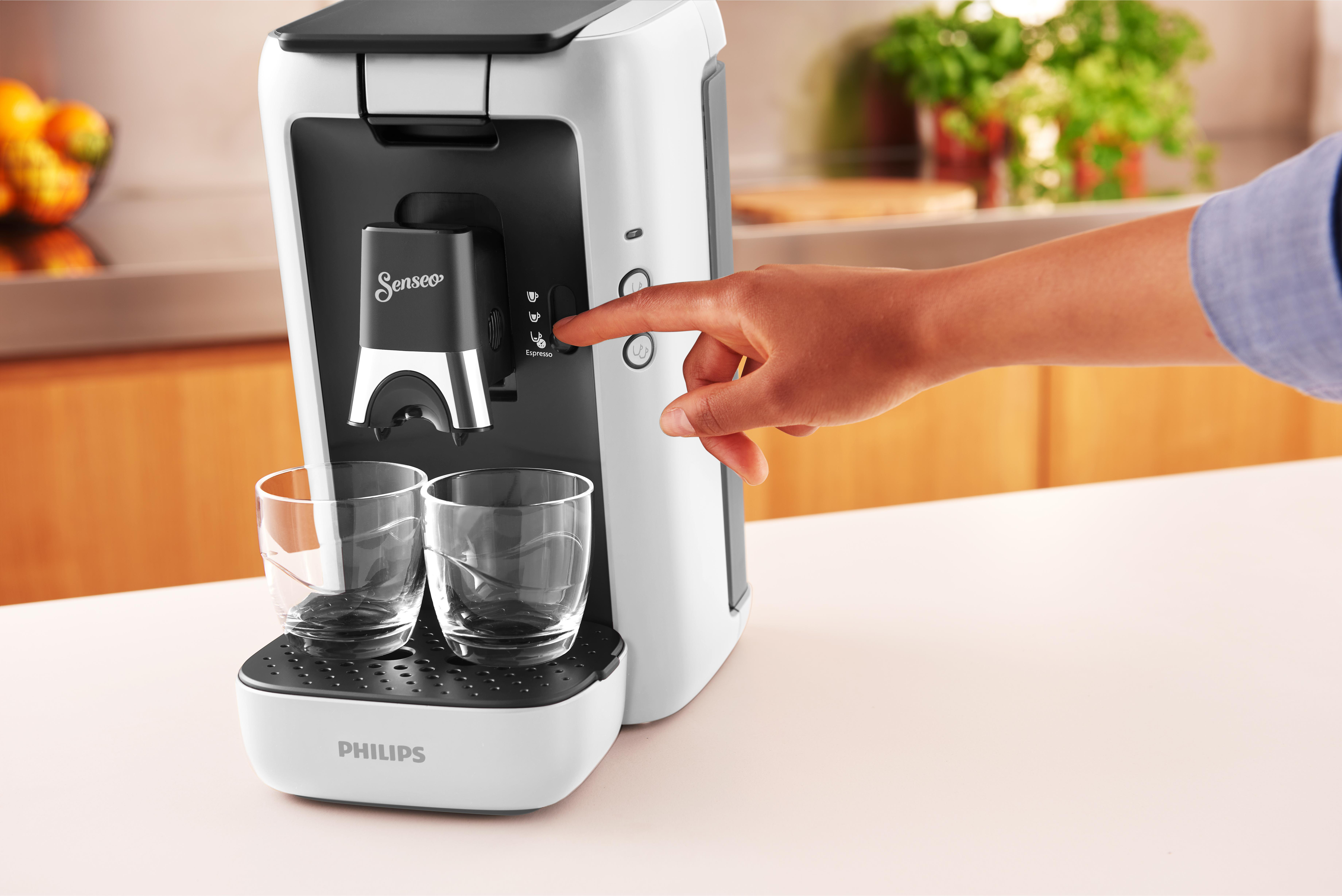 Eine Person drückt eine Taste an einer schwarz-weißen Kaffeemaschine. Leere Gläser darunter.