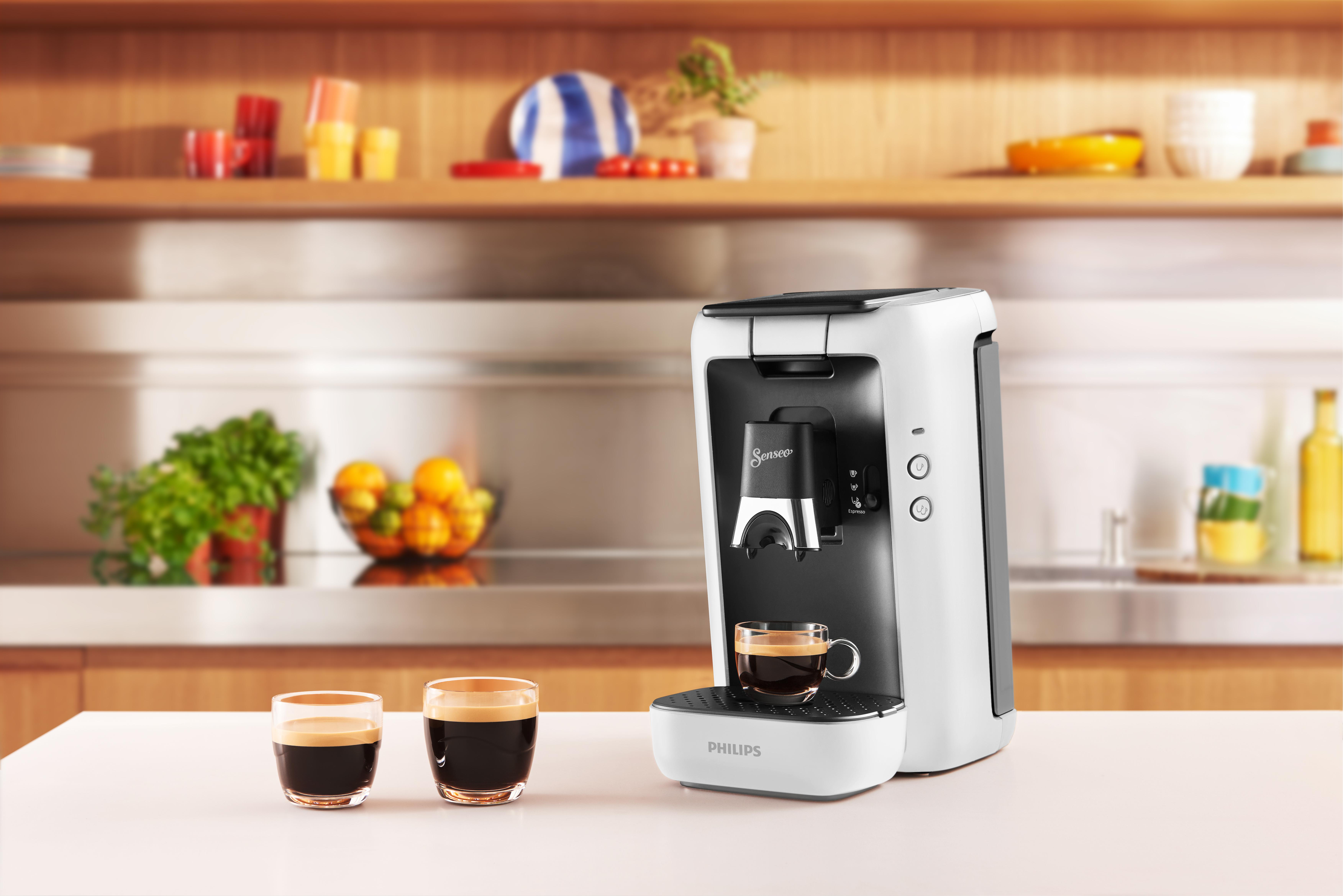 Eine weiße Kaffeemaschine mit schwarzem Deckel. Zwei Espresso und zwei Gläser stehen auf der Theke.