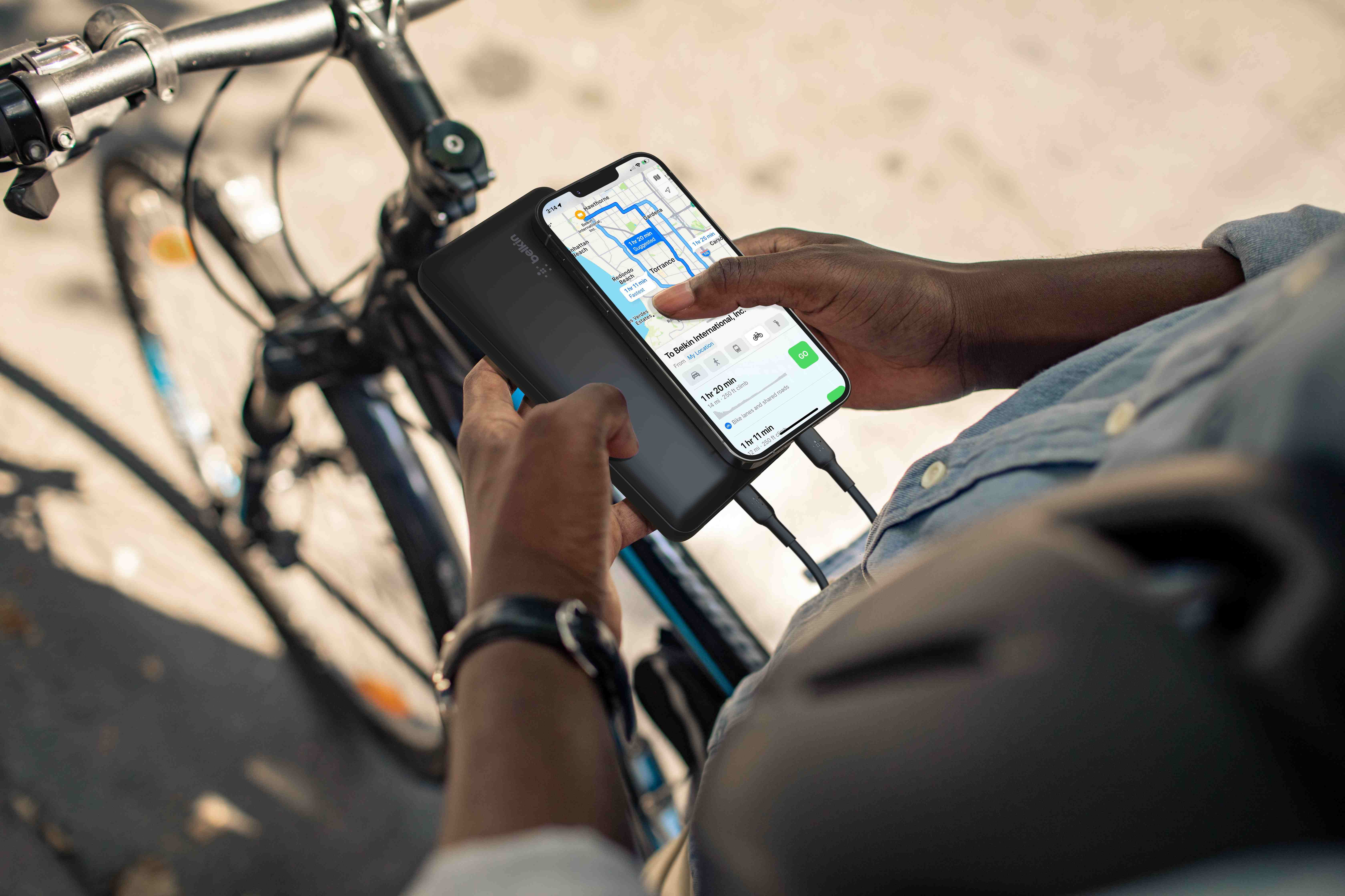 Personne avec un téléphone et une batterie externe près d'un vélo.