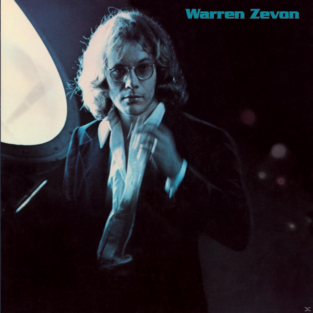Egy öltönyös férfi nyakkendőt tart egy fényes fény előtt. Felül Warren Zevon felirat látható.