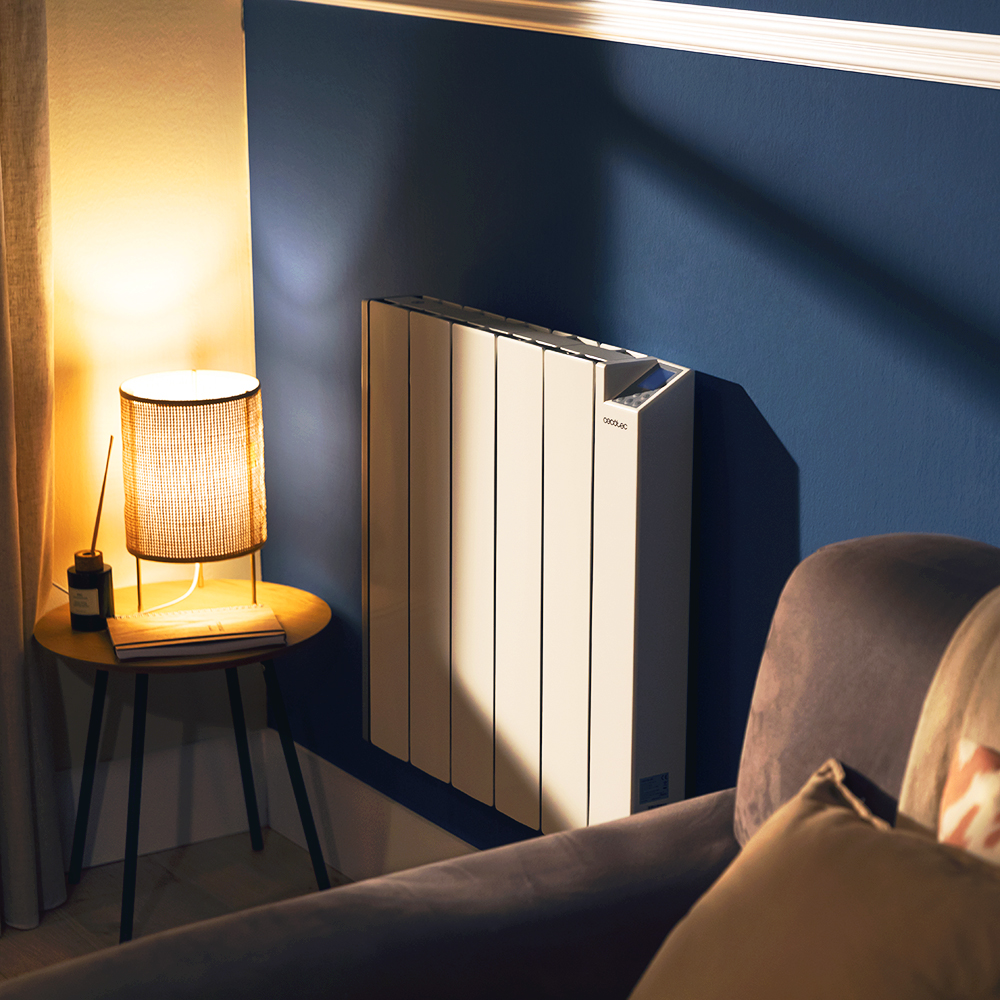 Un radiador eléctrico blanco en una pared azul, con una mesa y lámpara en primer plano.