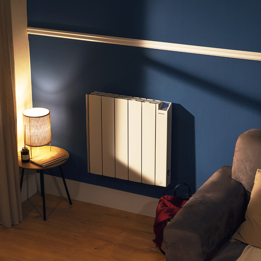 Un radiador beige en una pared azul. Una lámpara de mesa, una mesita con un libro y un sofá están en la habitación.