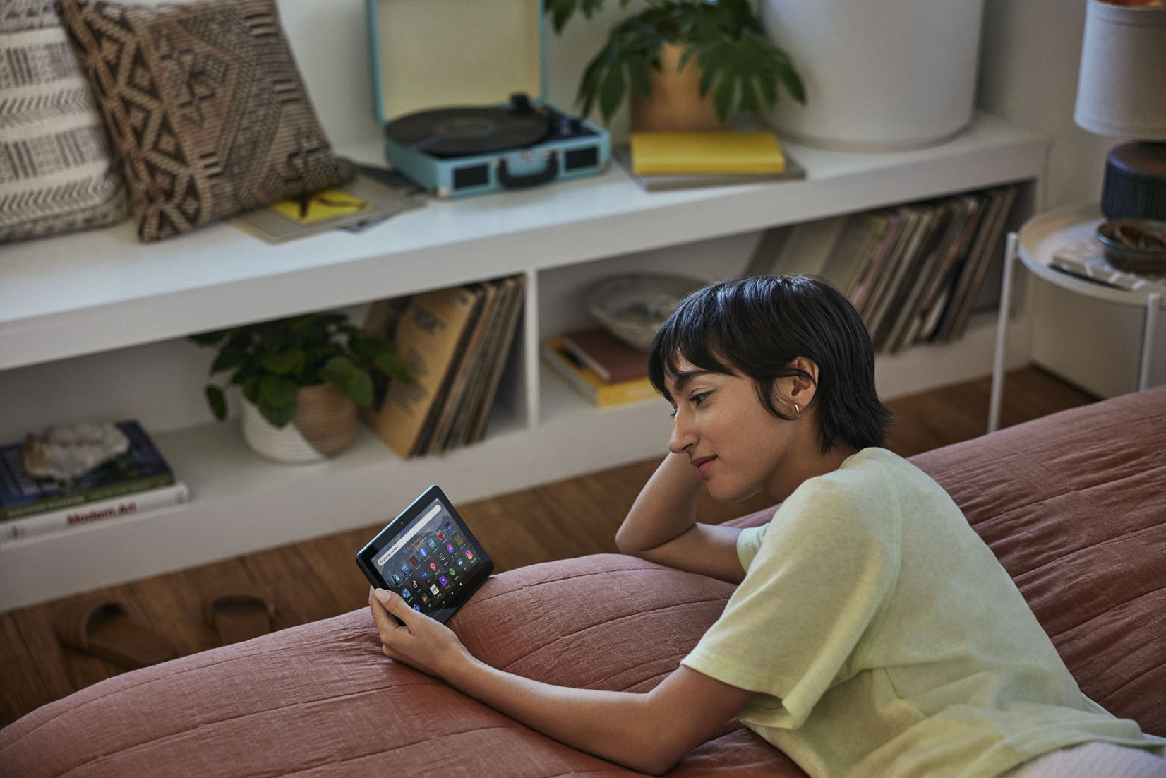 Frau liegt auf einem Bett und schaut auf ein Tablet, im Hintergrund ein Plattenspieler und Schallplatten.