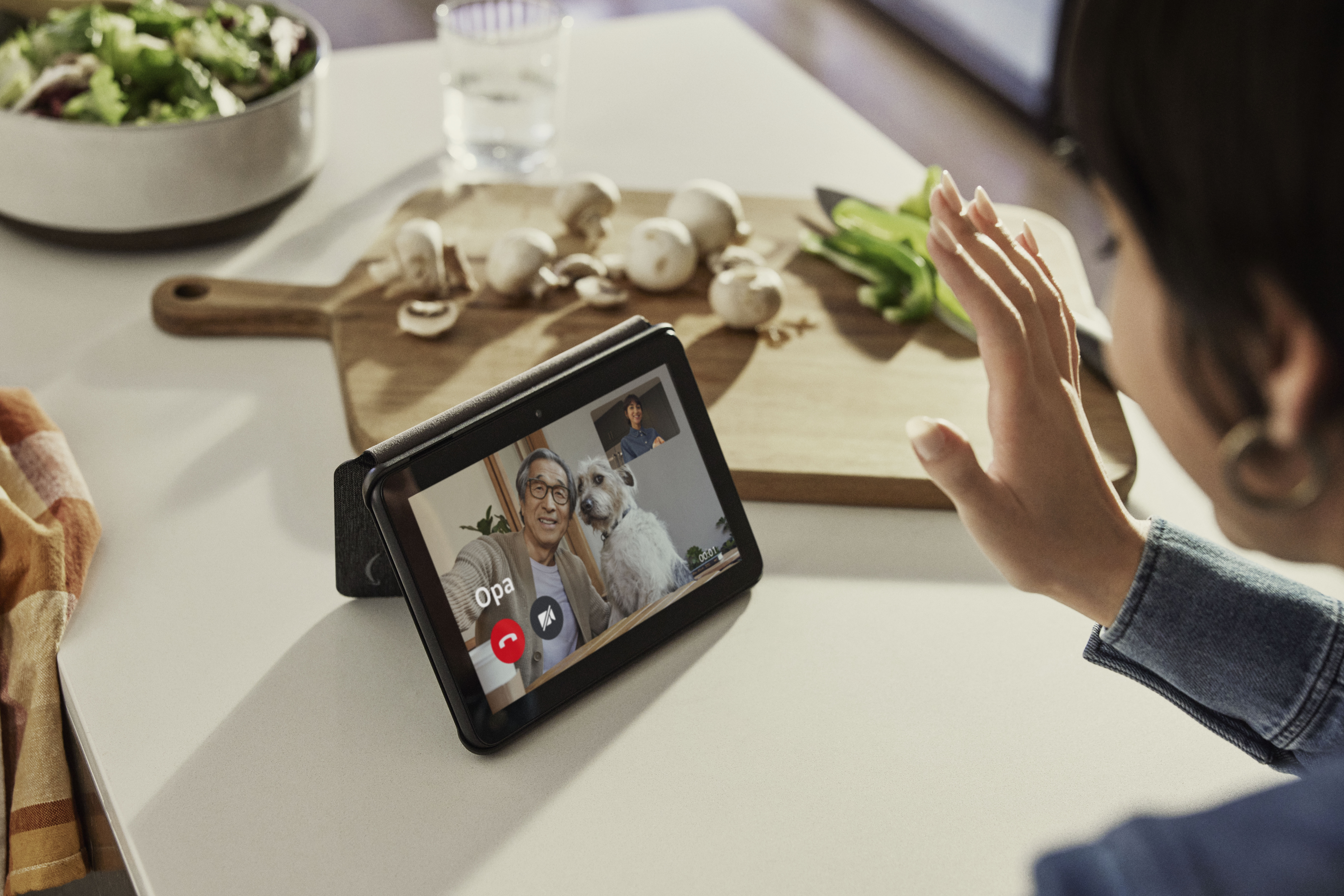 Tablet auf Tisch zeigt Videoanruf. Frau winkt, Mann und Hund im Bild.