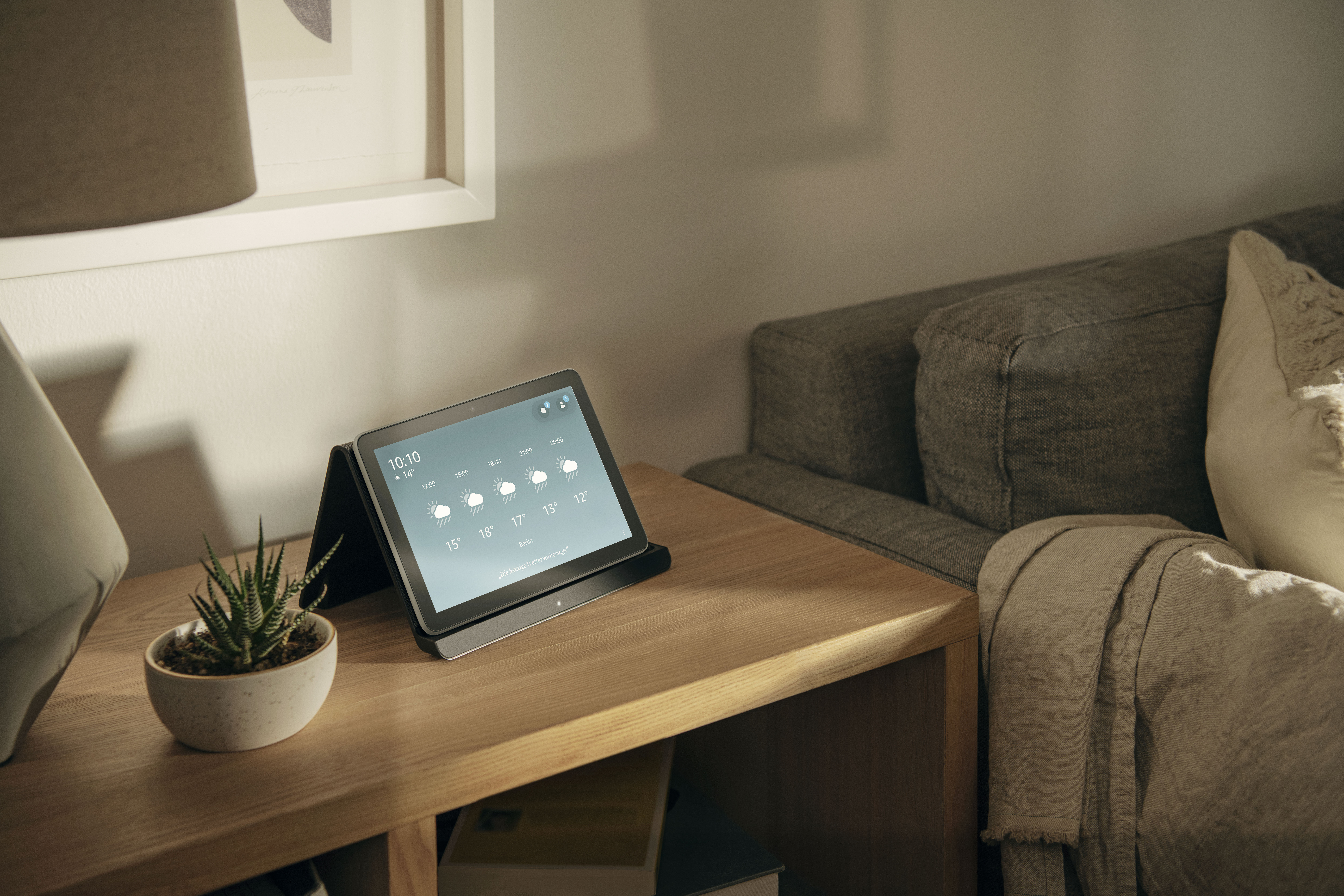 Tablet auf einem Holztisch, zeigt Wetterinformationen, mit Pflanze und Sofa.