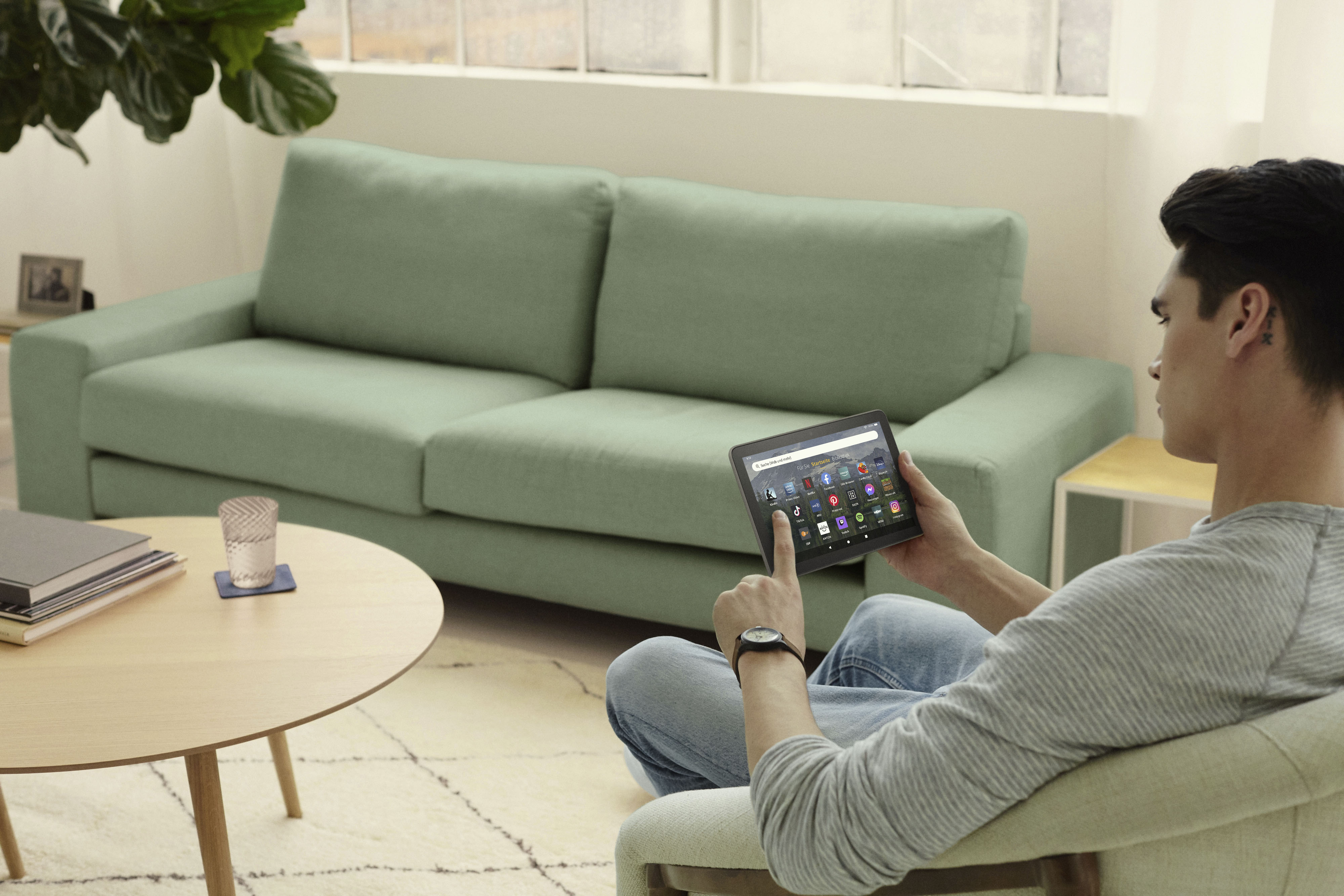 Mann benutzt Tablet, sitzt auf Couch, grüne Couch, Holztisch.