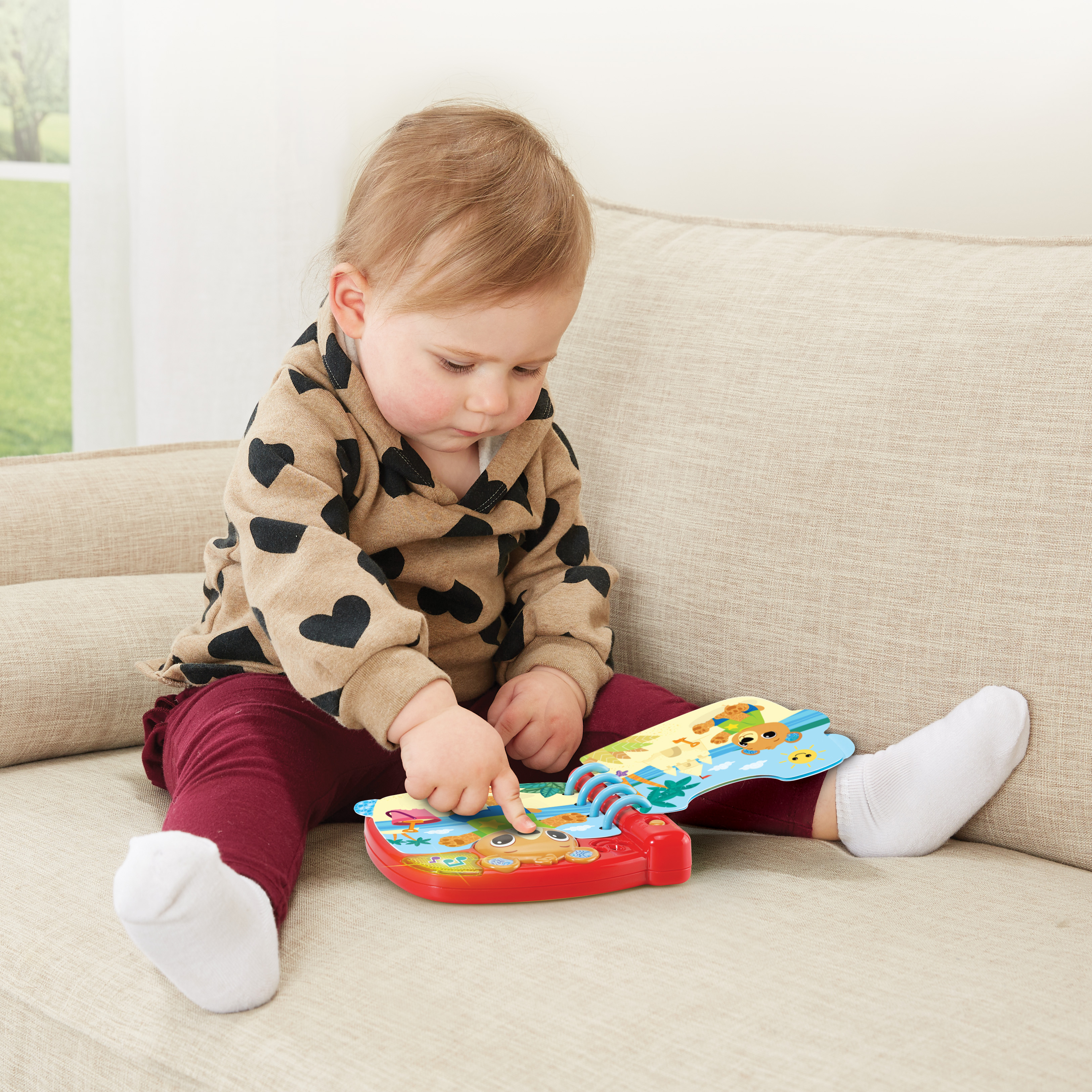 Ein Baby sitzt auf einer Couch und spielt mit einem Spielzeugbuch.