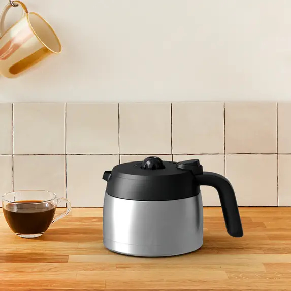 Een zilveren en zwarte koffiepot met een kopje koffie.